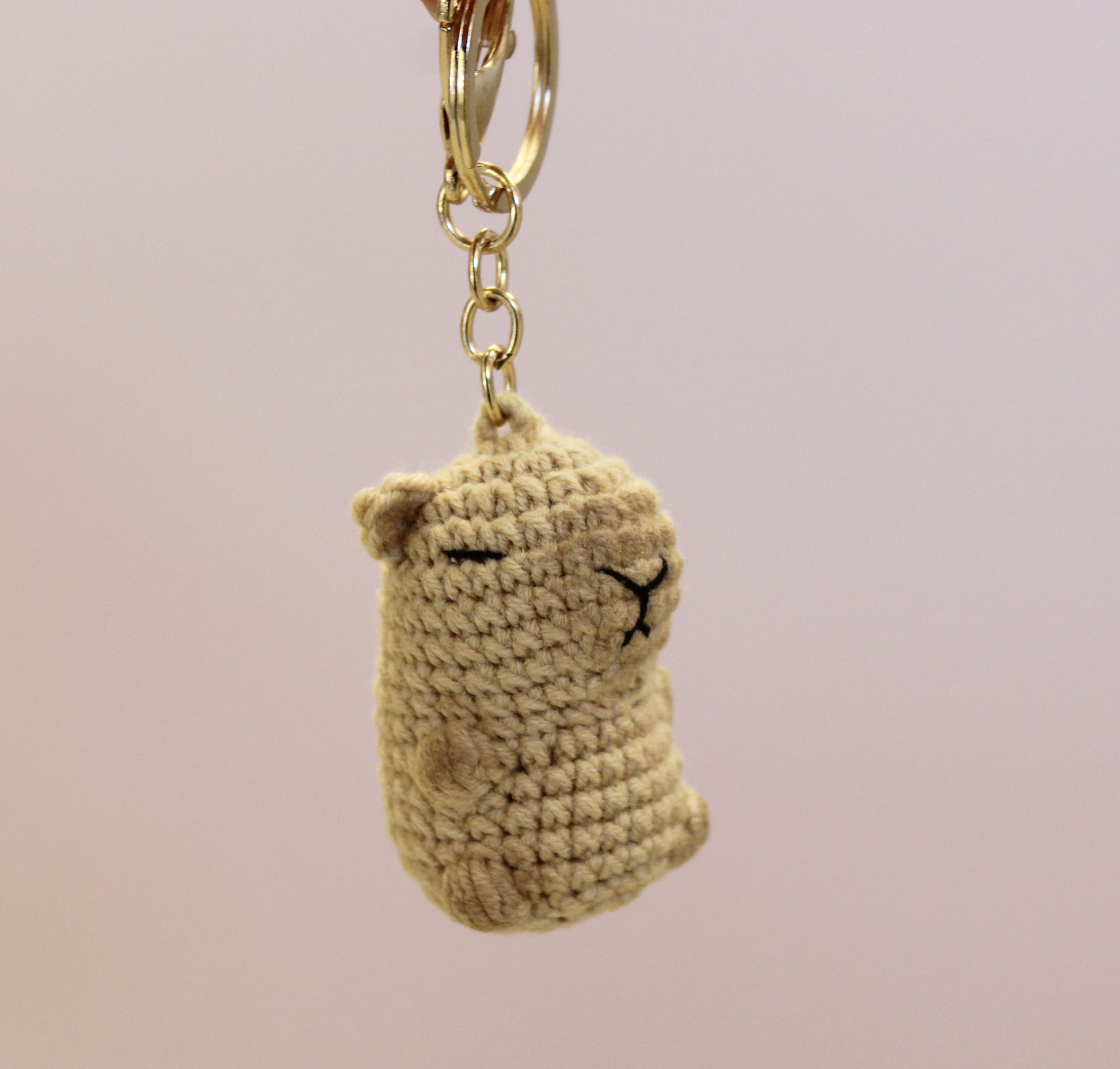 Handmade crochet capybara keychain in beige with a gold-colored metal ring and chain.