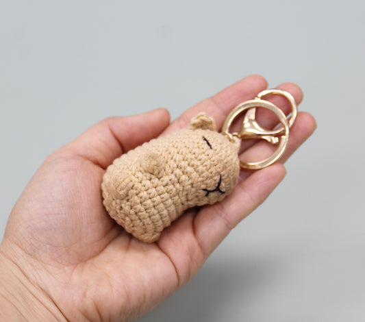Handmade crochet capybara keychain in beige with a gold-colored metal ring and embroidered facial features.