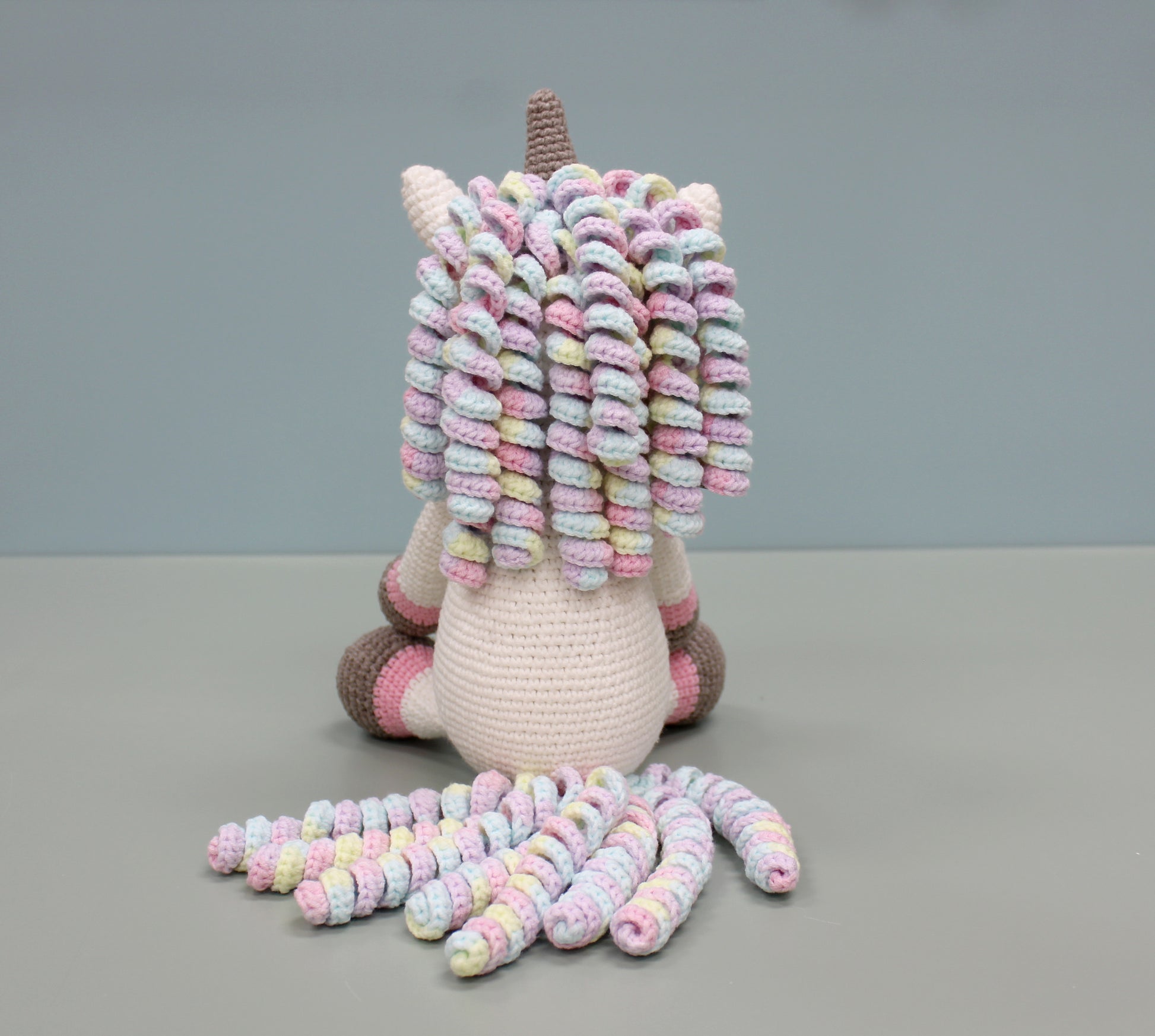 Handmade crochet unicorn plush with multicolored spiraled mane, tail, and pastel accents.