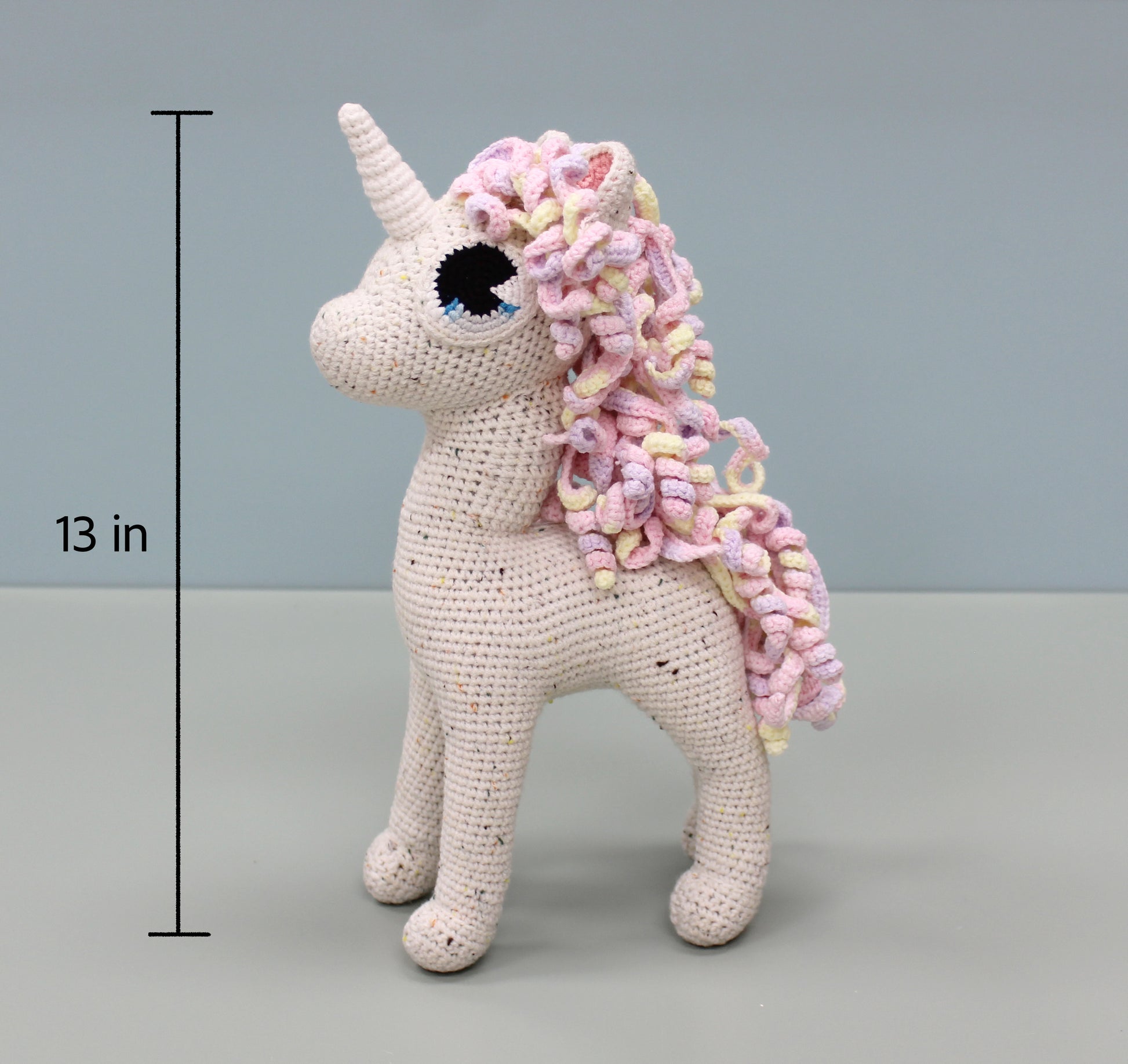 Handmade crochet unicorn stuffed animal with colorful curly mane and white speckled body, 13 inches tall.