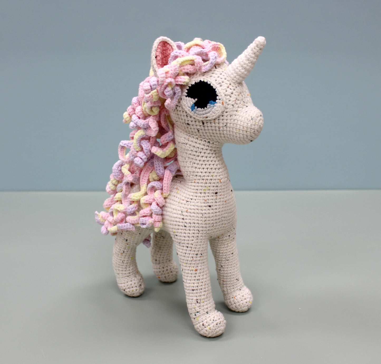 Handmade crochet unicorn stuffed animal with colorful speckled yarn, featuring a multicolored mane and horn.