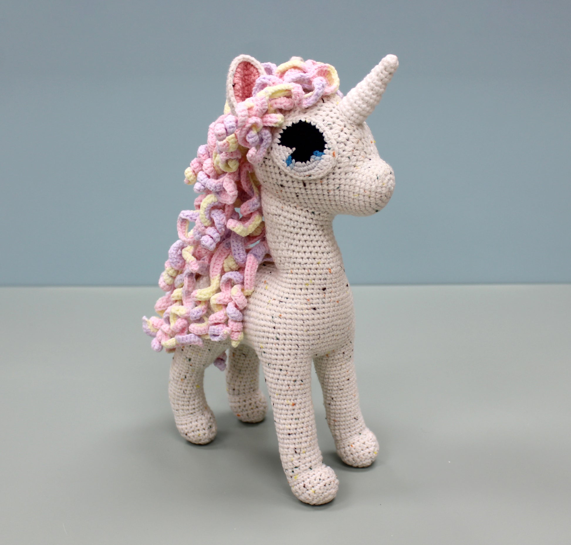 Handmade crochet unicorn stuffed animal with colorful speckled yarn, featuring a multicolored mane and horn.