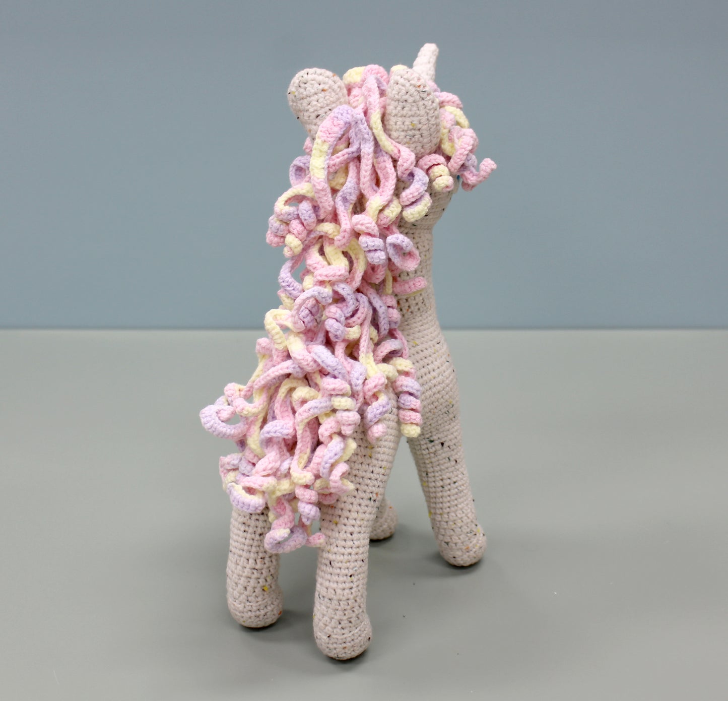 Handmade crochet unicorn stuffed animal with colorful curly mane and speckled body, 13 inches tall.