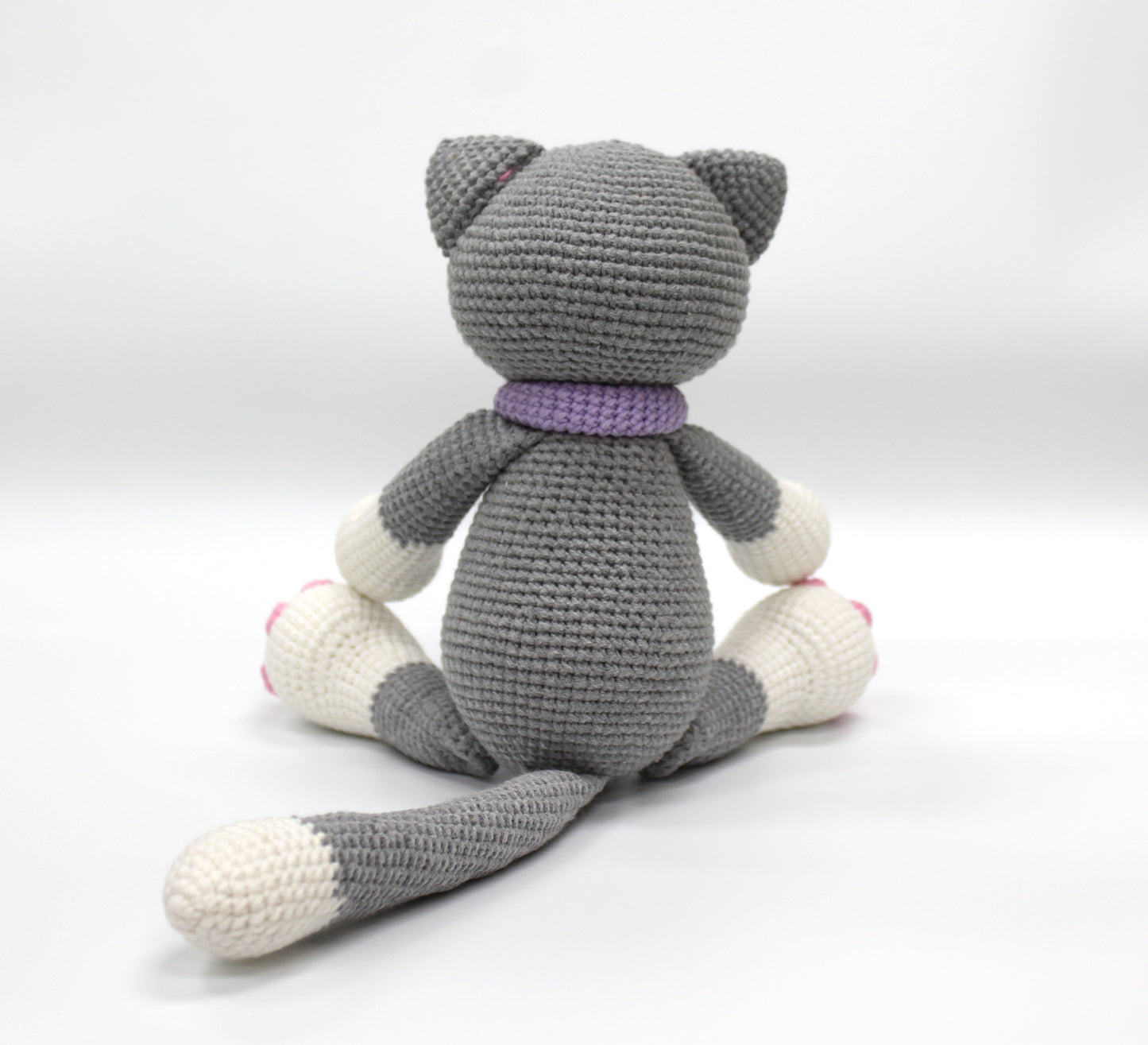 Gray and white crochet stuffed cat with a purple collar and pink paw pads.