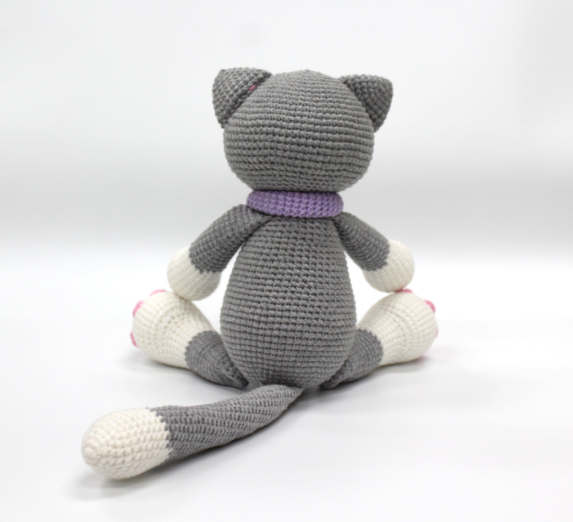 Gray and white crochet stuffed cat with a purple collar and pink paw pads.