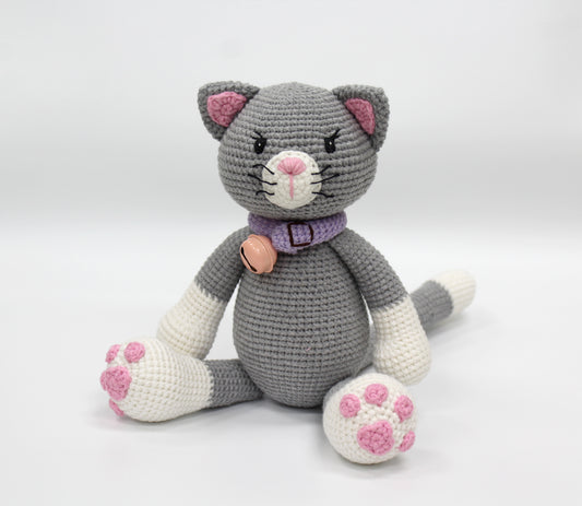 Gray and white crochet stuffed cat with pink paw pads, a purple collar, and a small bell.
