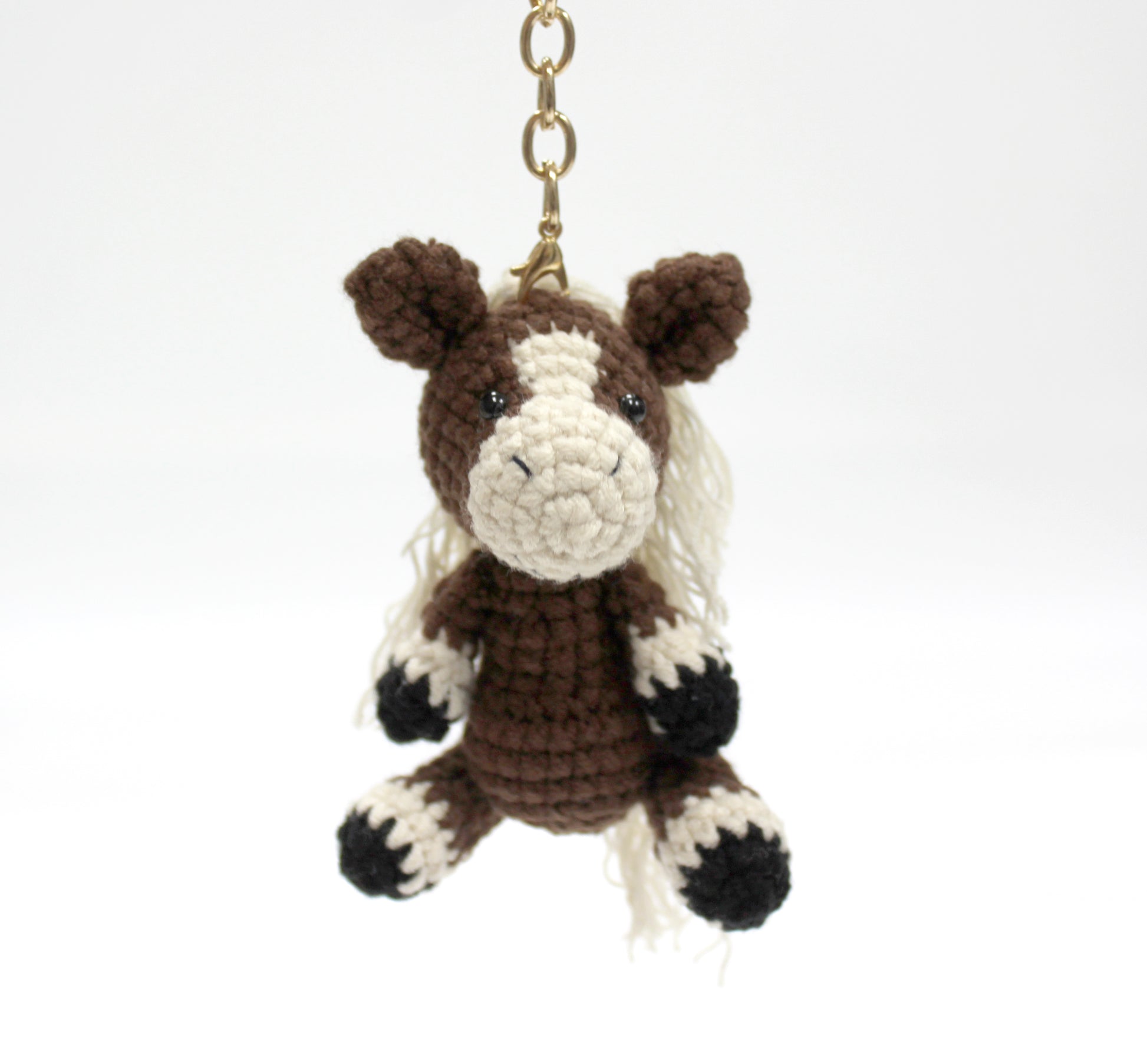 Brown and white handmade crochet horse keychain with black hooves, attached to a gold chain.