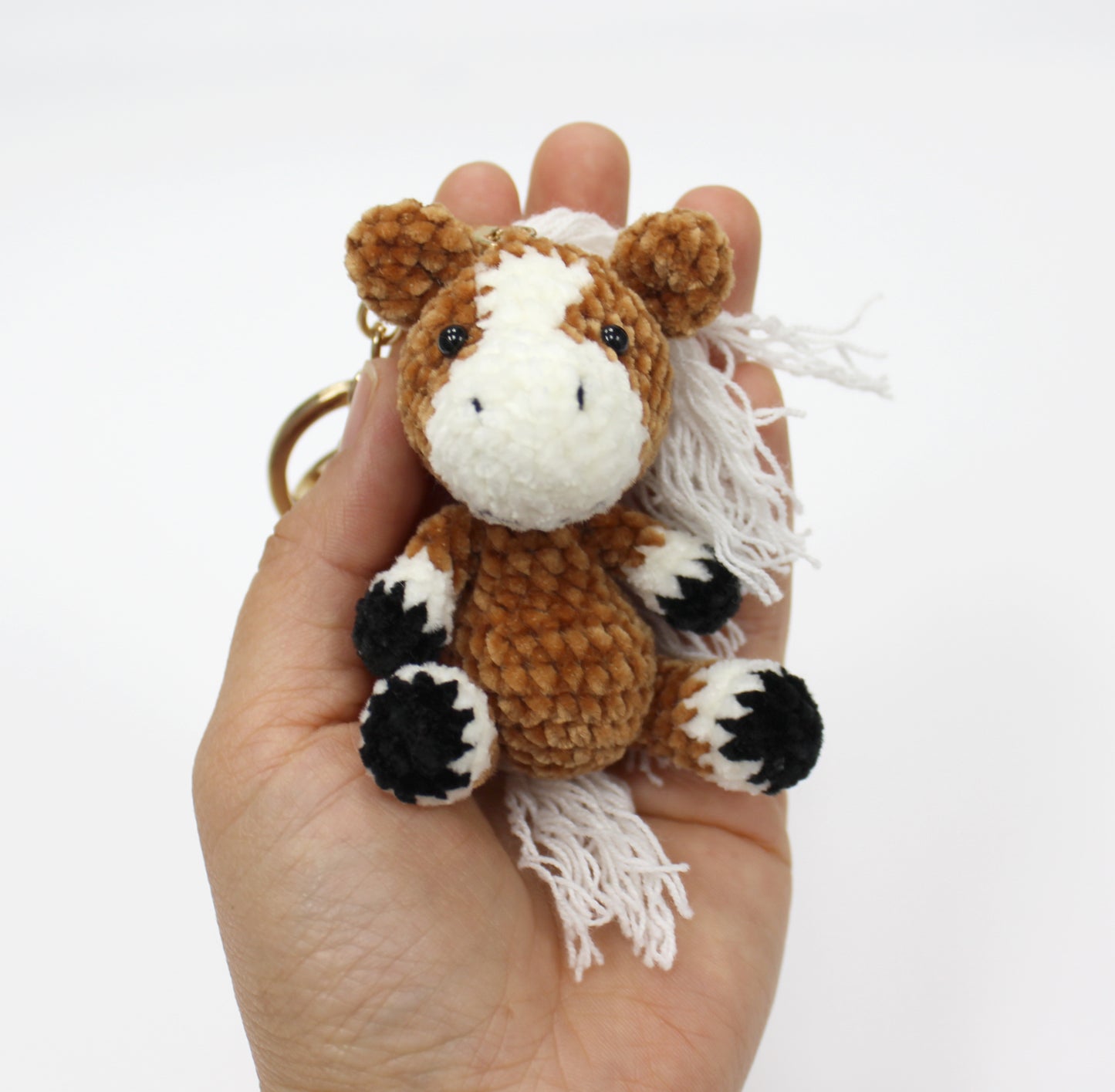 Brown and white handmade crochet horse keychain with black hooves, approximately 3 inches tall.