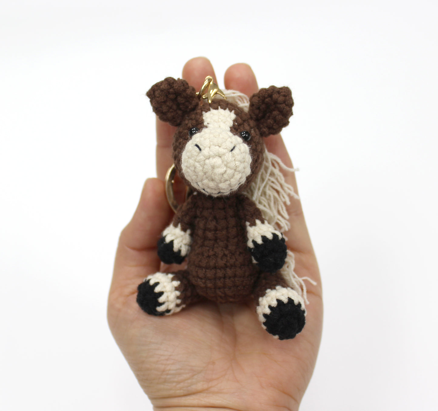 Brown and white handmade crochet horse keychain with black hooves, approximately 3 inches tall.