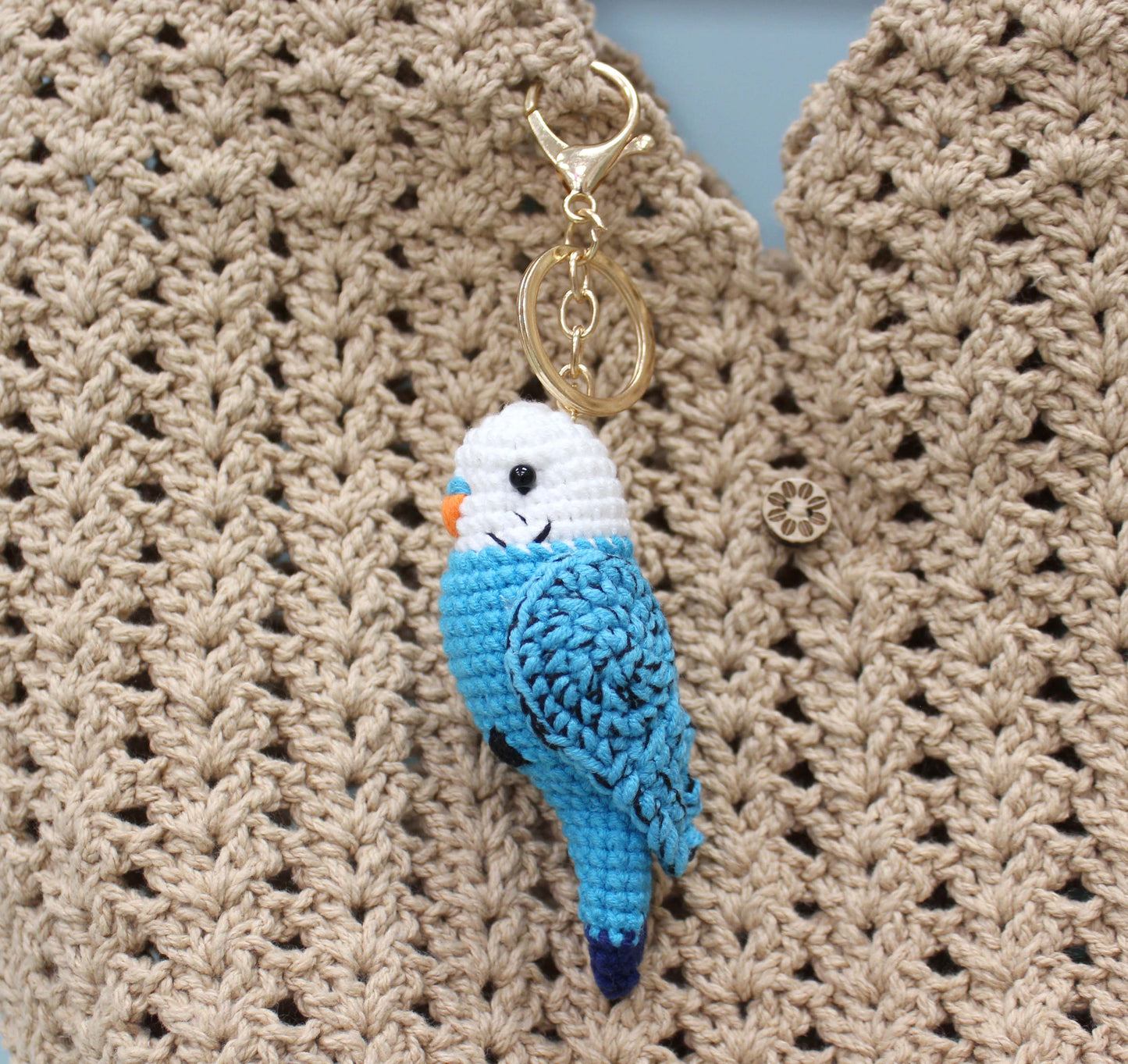 Handmade crochet keychain shaped like a blue and white parakeet with a gold ring.