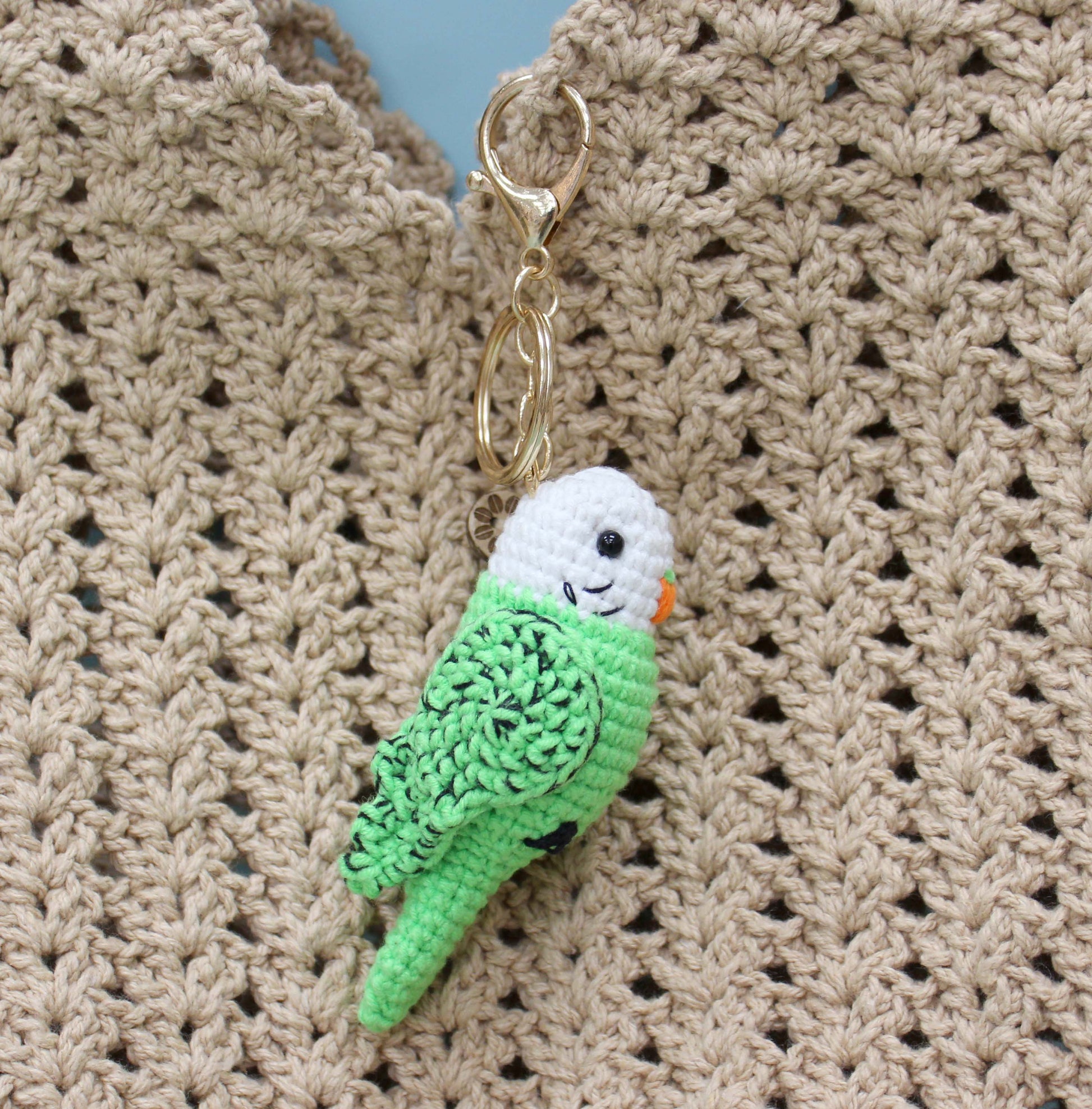 Handmade crochet keychain shaped like a green and white parakeet with a gold ring.