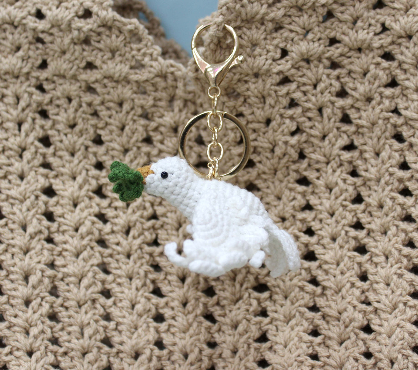Handmade white crochet dove keychain holding a green leaf, with a gold-toned ring.