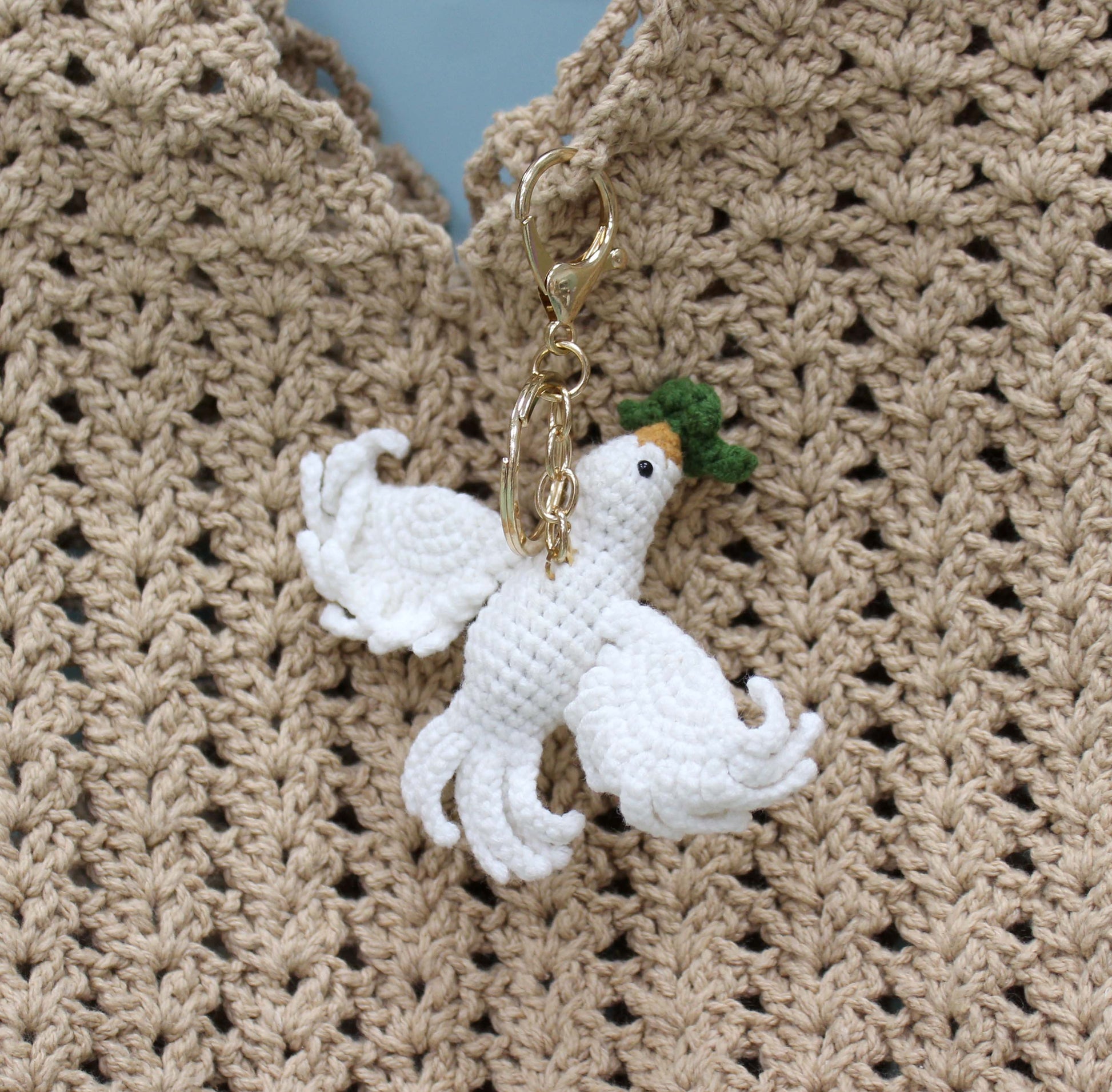 Handmade white crochet dove keychain with green hat and gold hardware.