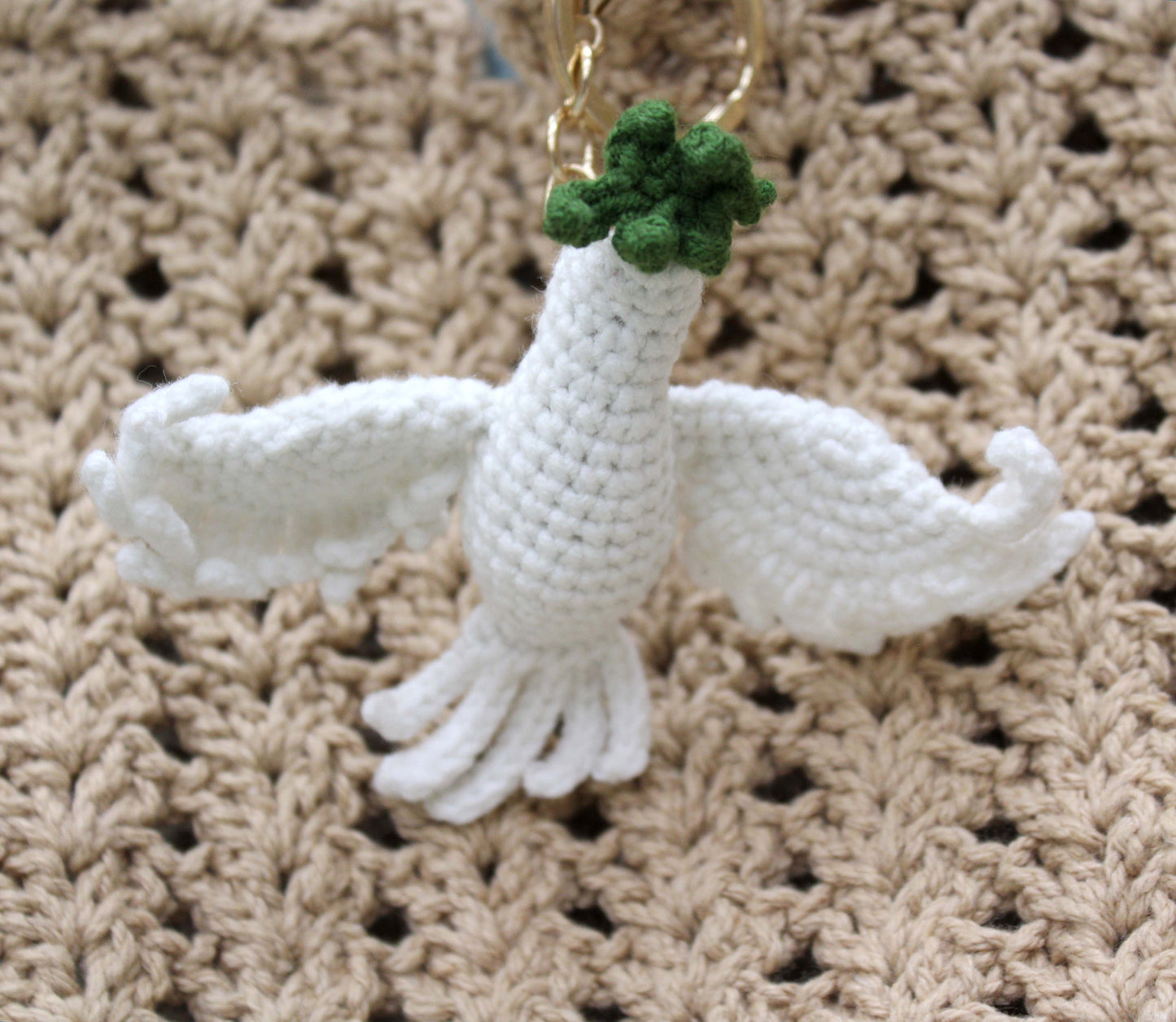 Handmade white crochet dove keychain with green accents and gold chain.