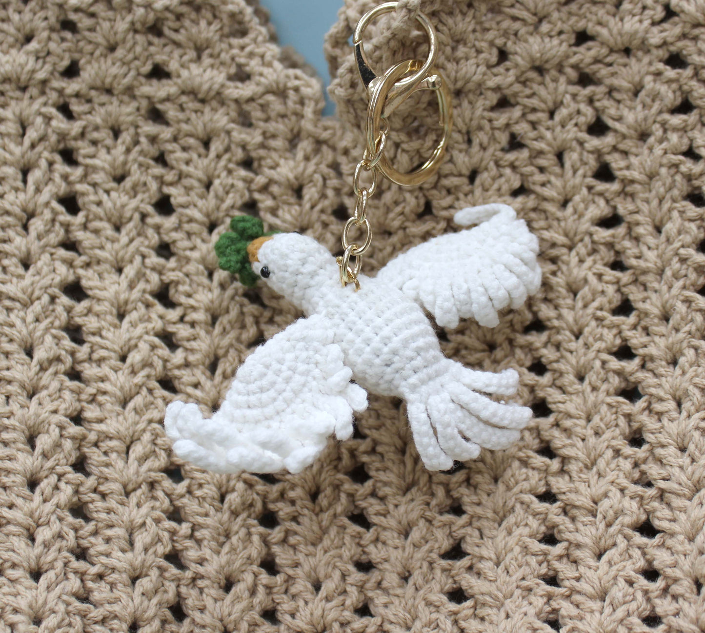 Handmade white crochet dove keychain with green and orange accents, attached to a gold ring.