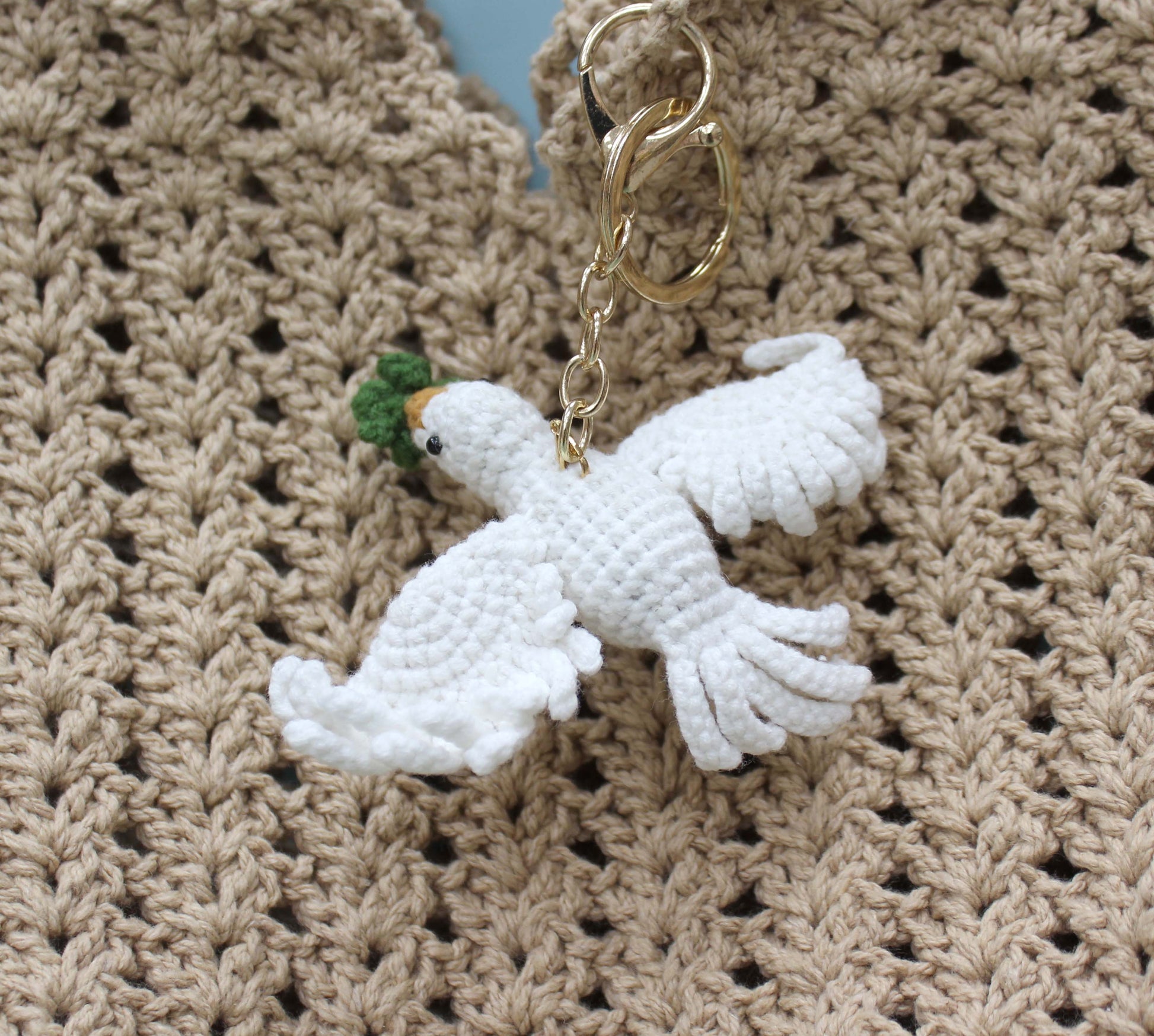 Handmade white crochet dove keychain with green and orange accents, attached to a gold ring.
