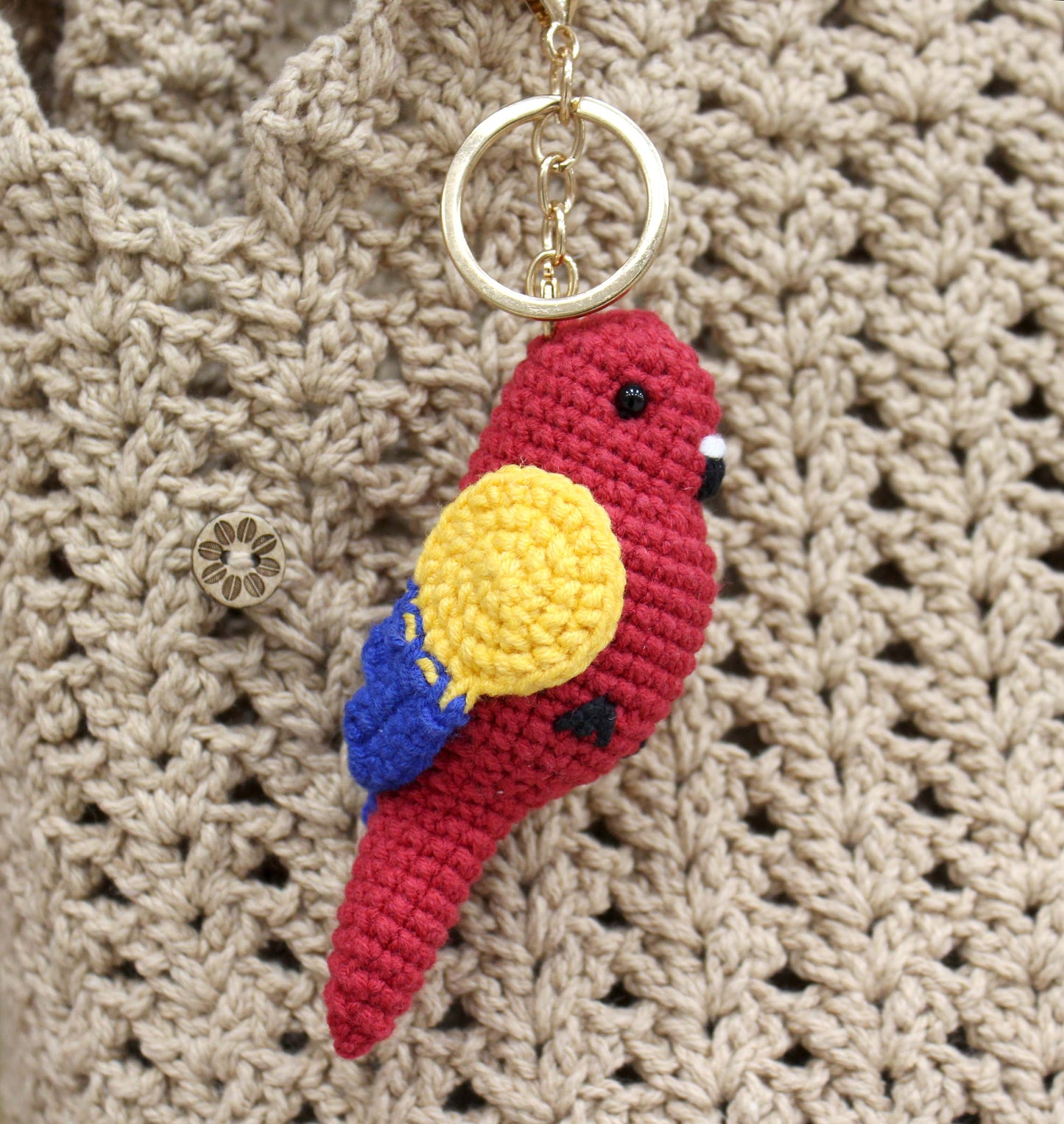 Handmade crochet bird keychain in red with yellow wing accents, attached to a gold ring.