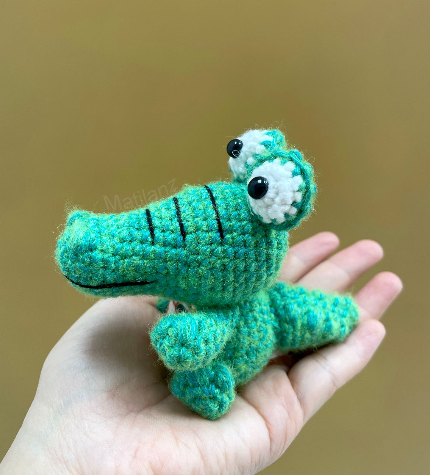 A small, crocheted green gator keychain with white accents and black bead eyes.
