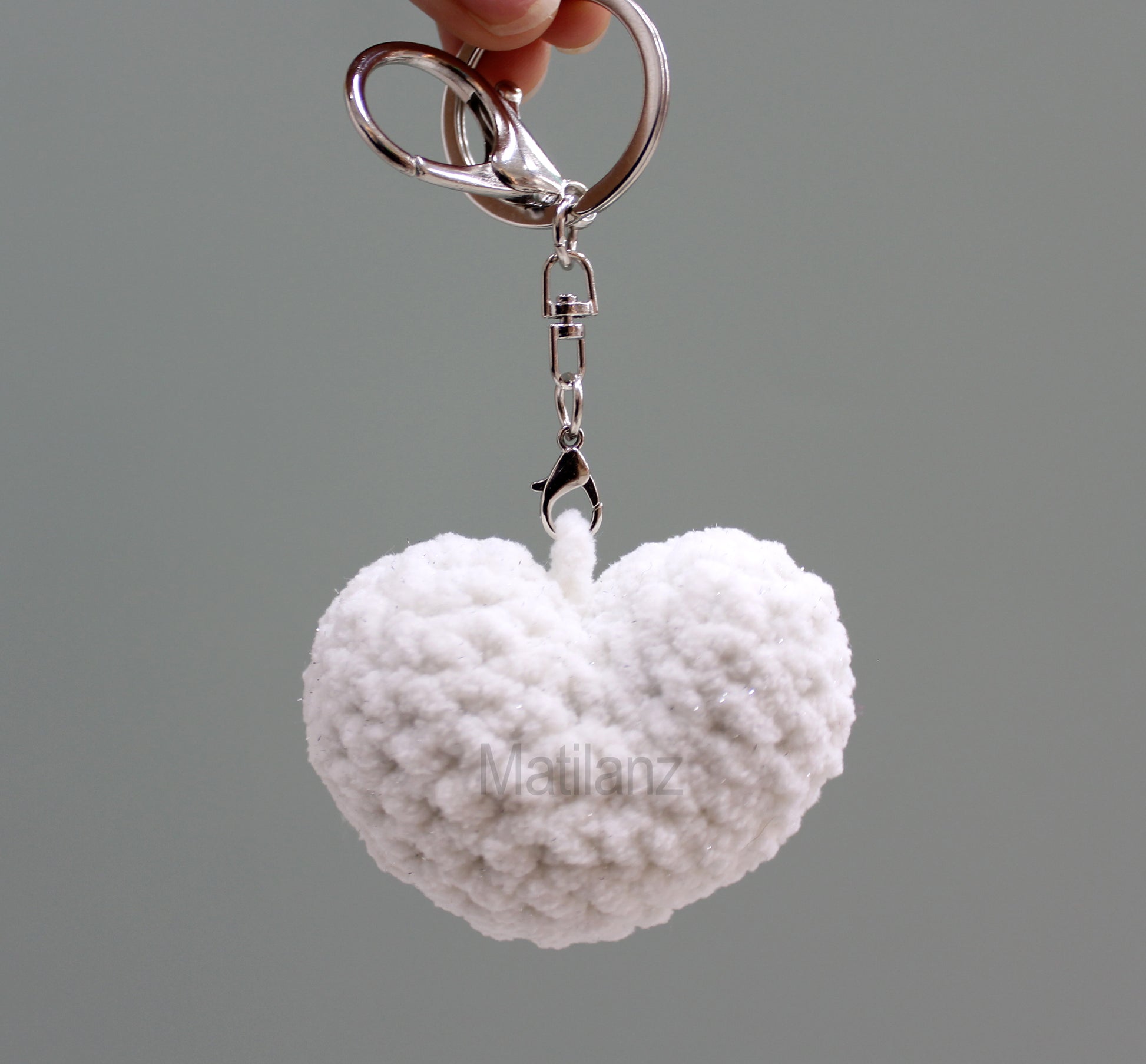 A handmade crochet heart keychain in white, featuring a fluffy texture and a silver ring.