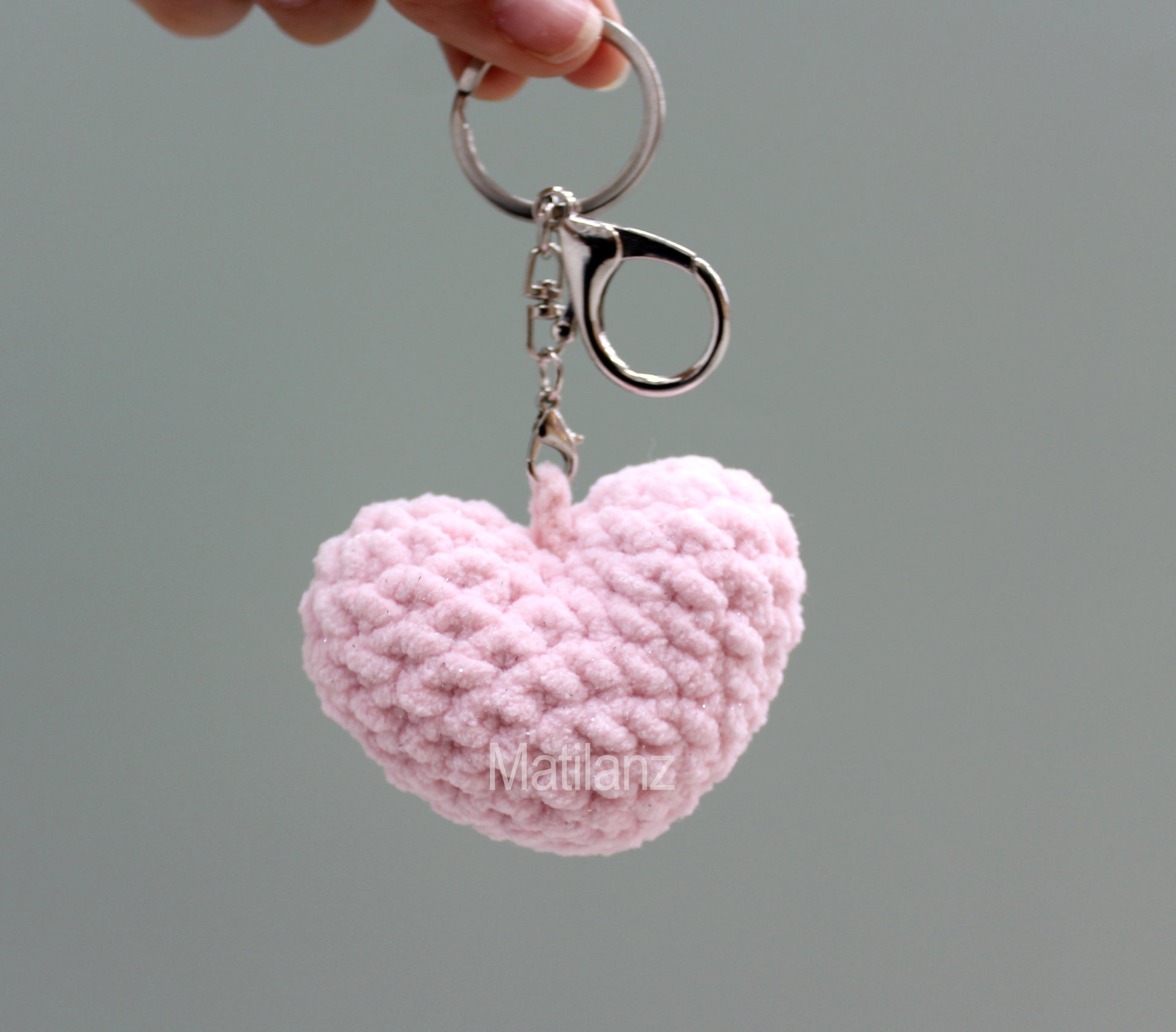 A delicate pink crocheted heart keychain with a metallic ring.