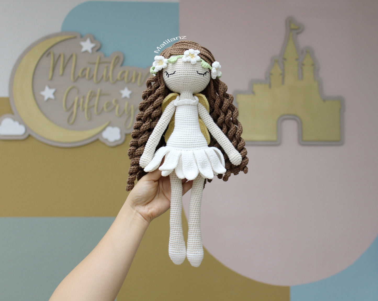 A handmade crochet fairy doll with long brown braids, white dress, and flower crown, 15 inches tall.