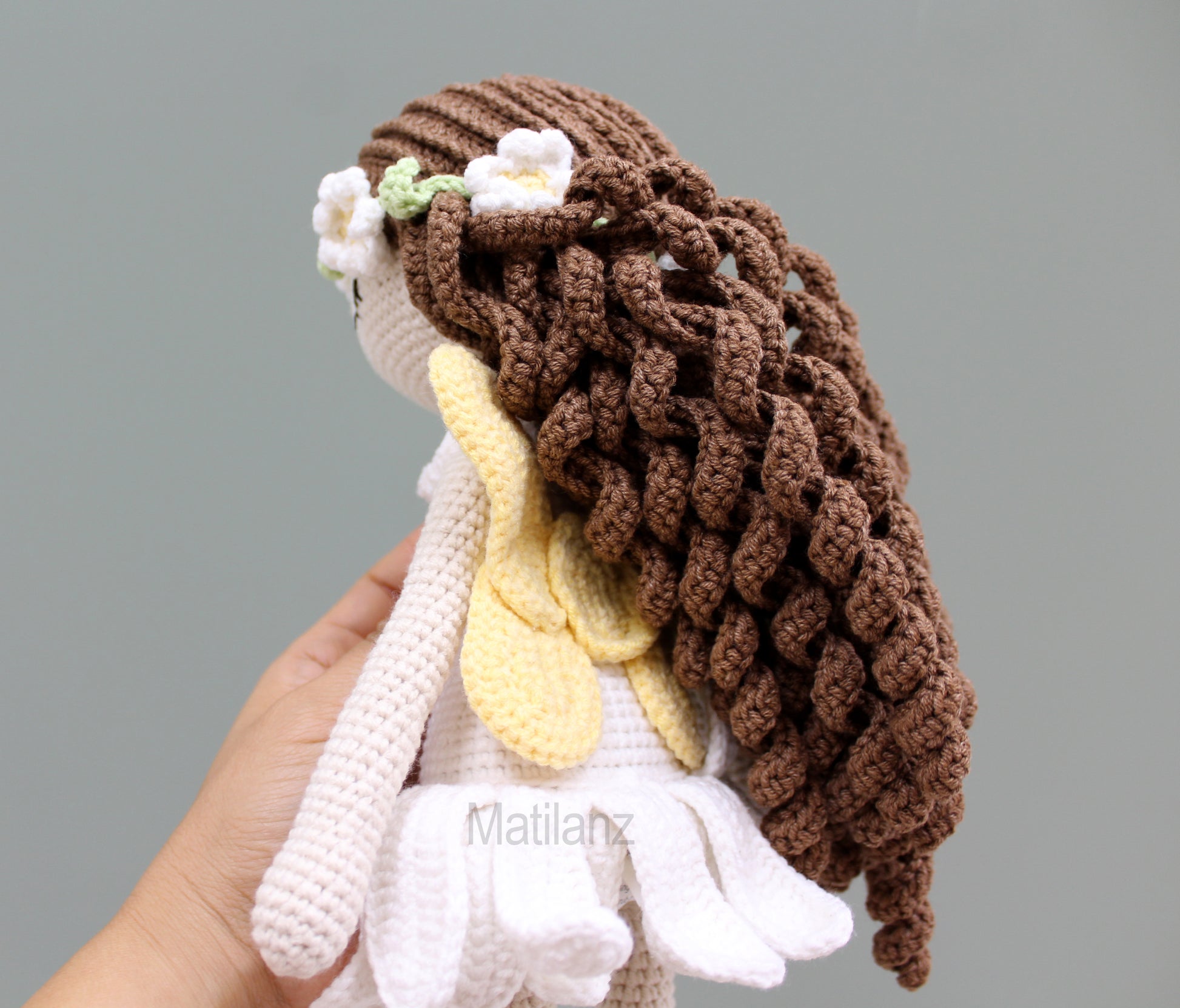 A handmade crochet fairy doll with long brown hair, white dress, and yellow wings.