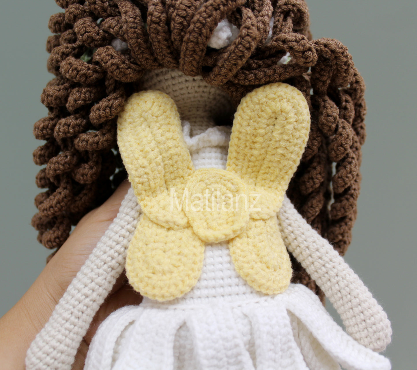 A handmade crochet fairy doll with brown hair, white dress, and yellow wings.