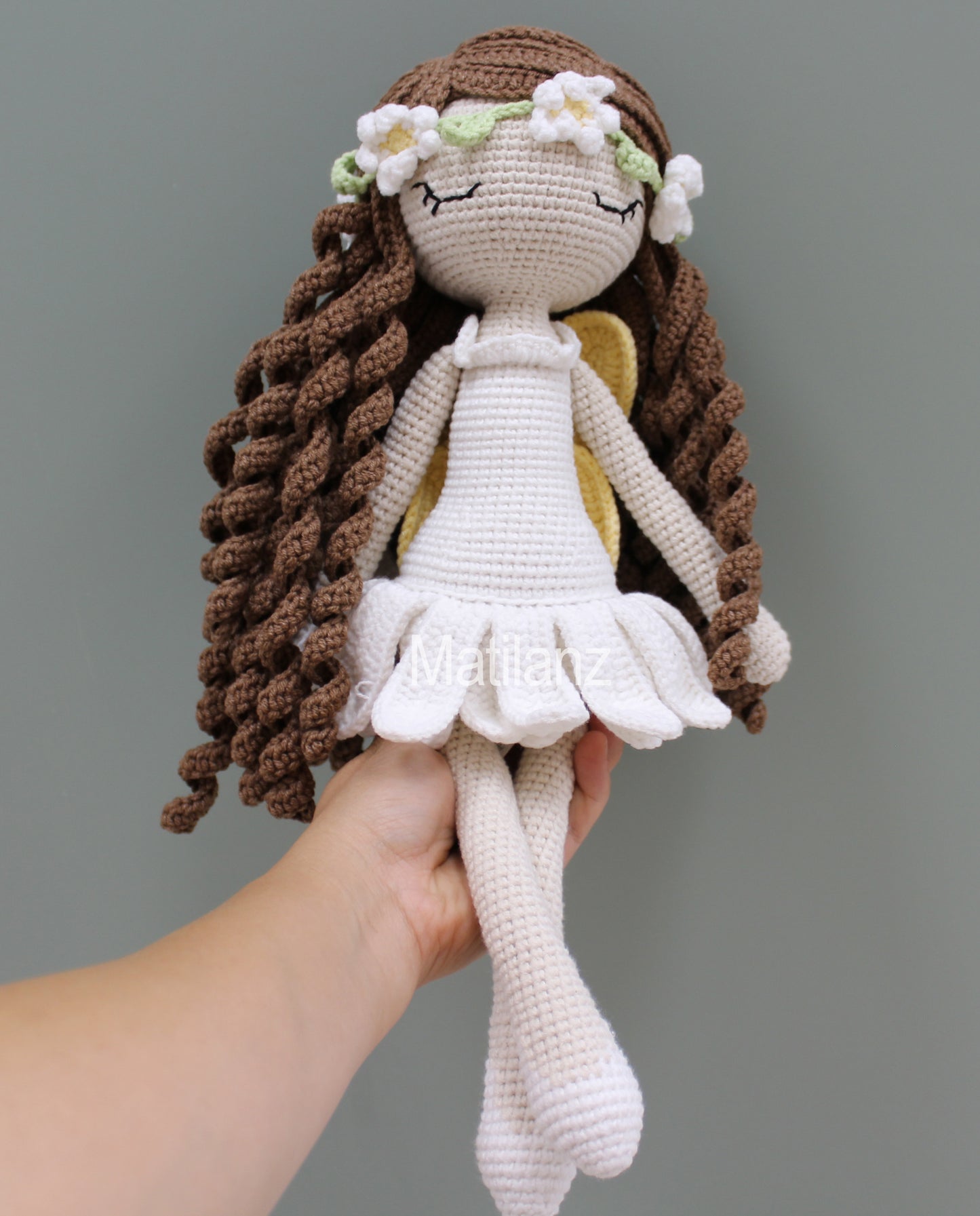 A handmade crochet fairy doll with long brown braids, white dress, and flower crown.
