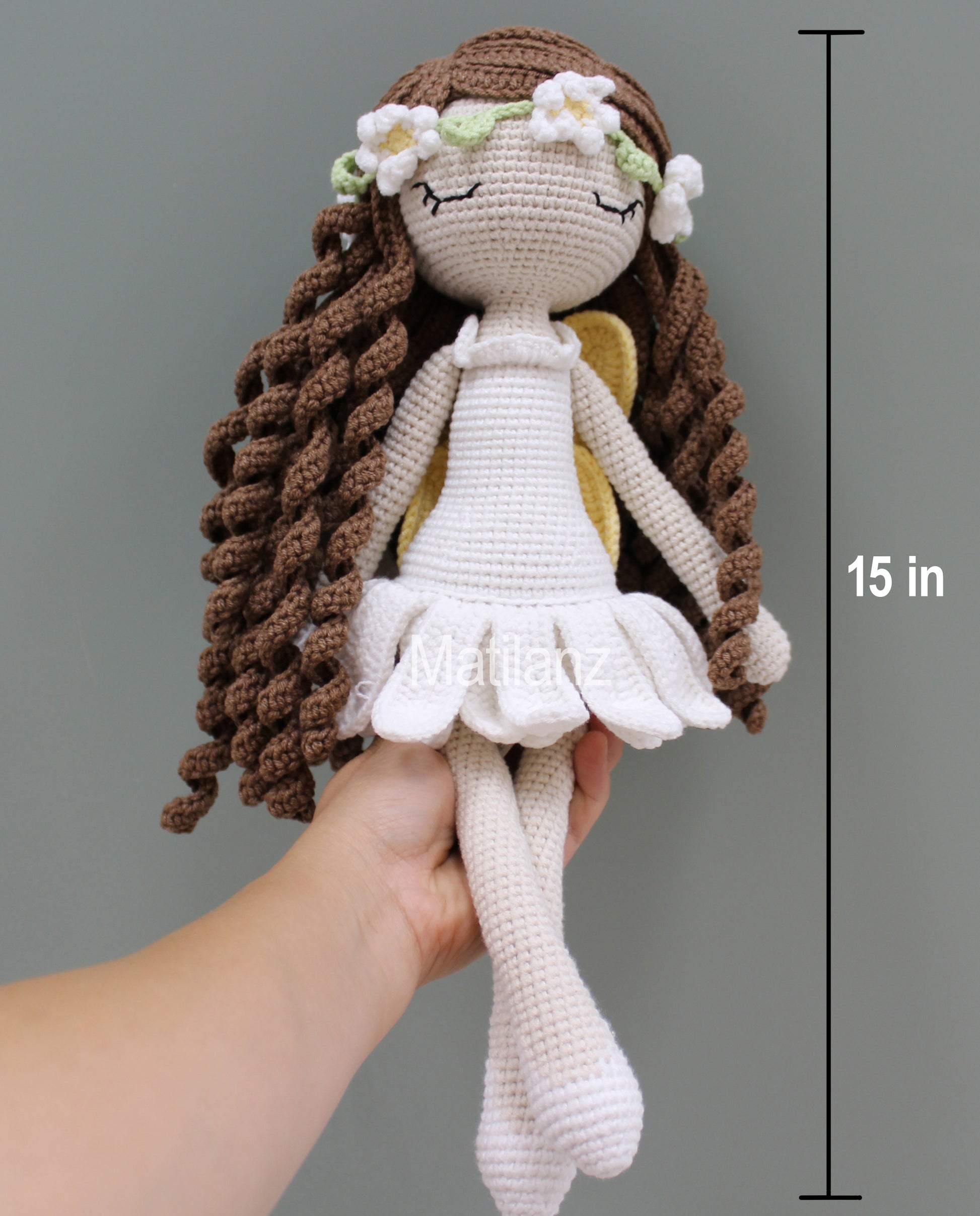 A handmade crochet fairy doll with long brown braids, white dress, and flower crown, 15 inches tall.