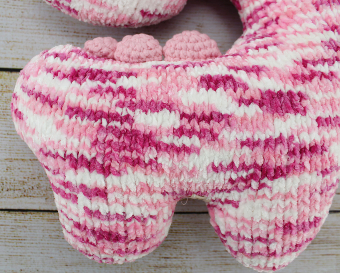 Handmade crochet dinosaur neck pillow in pink and white stripes with rounded ears.