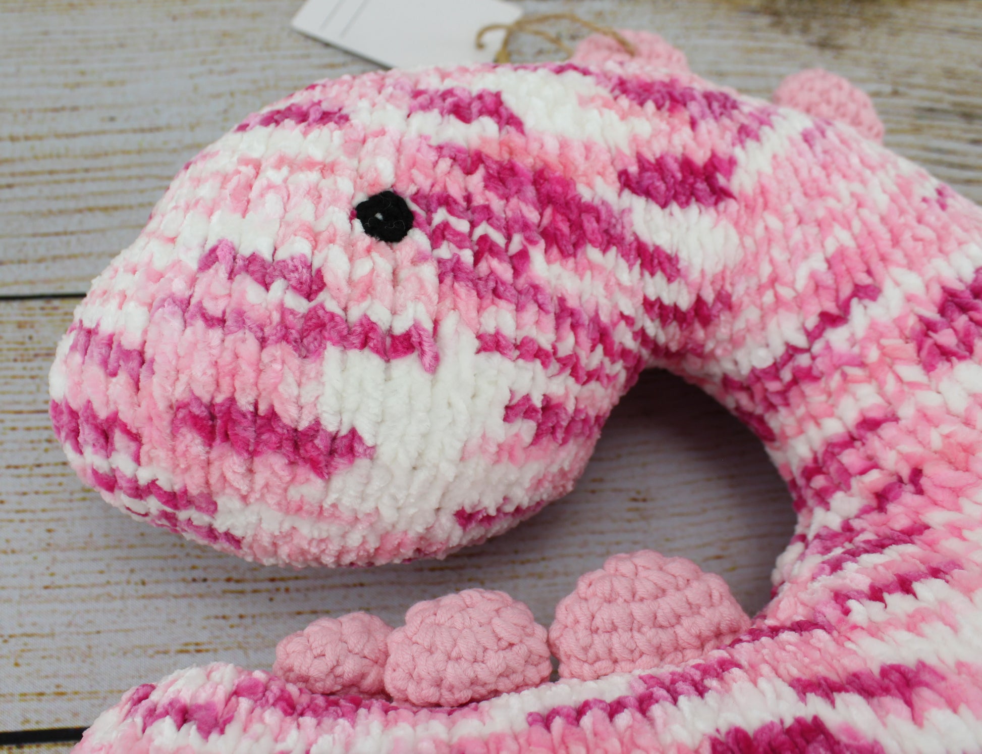 Handmade pink and white crochet dinosaur neck pillow with soft texture and small legs.