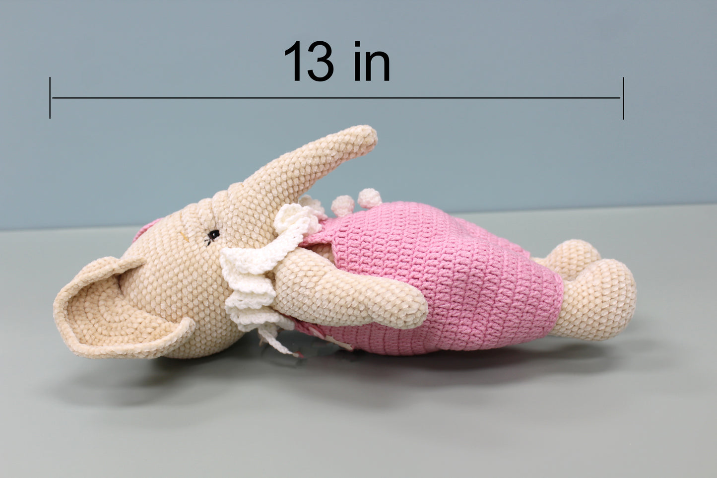 A handmade crochet elephant wearing pink overalls, 13 inches long.