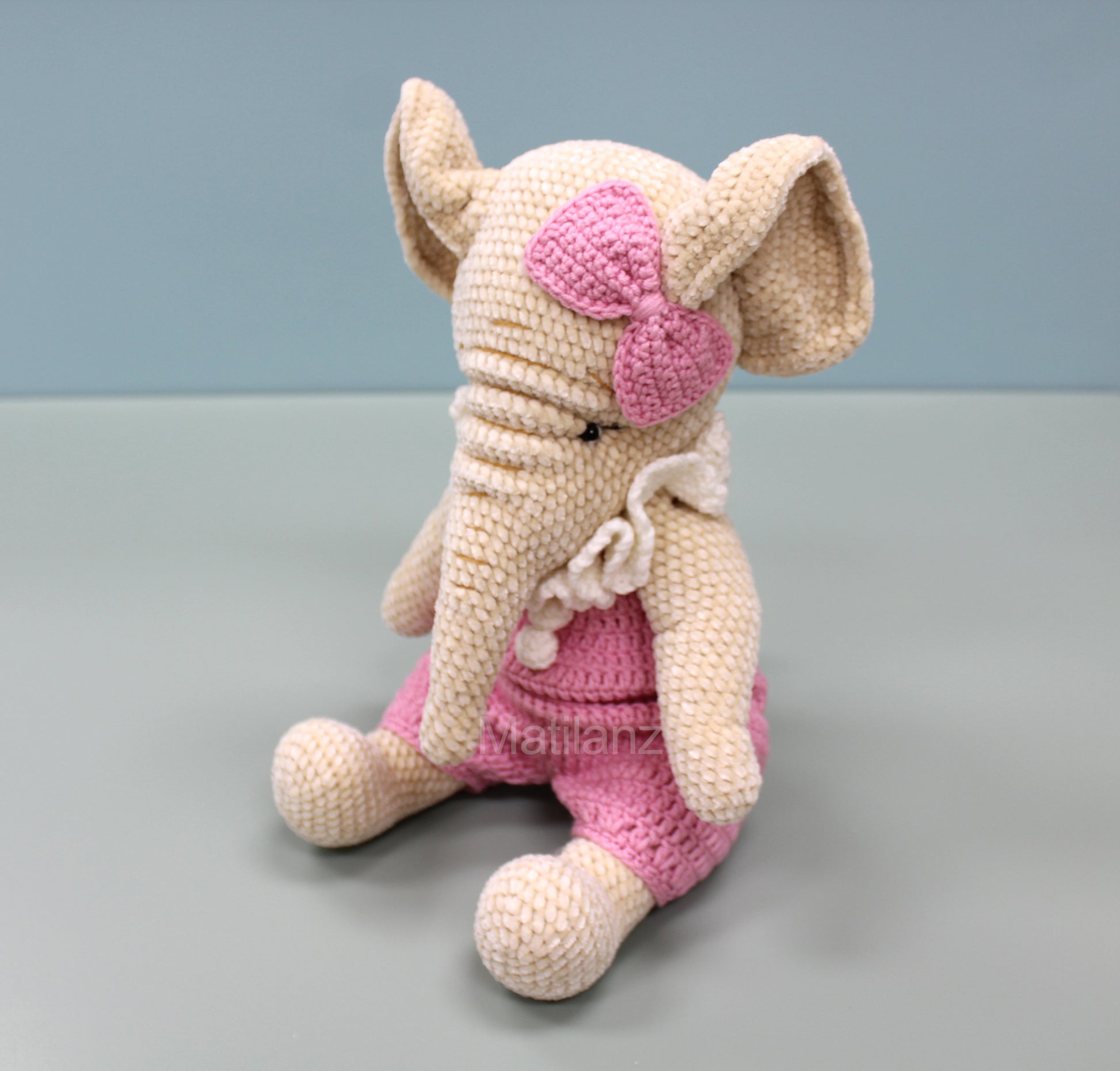 Crochet elephant in pink overalls with a pink bow, handmade and charmingly detailed.