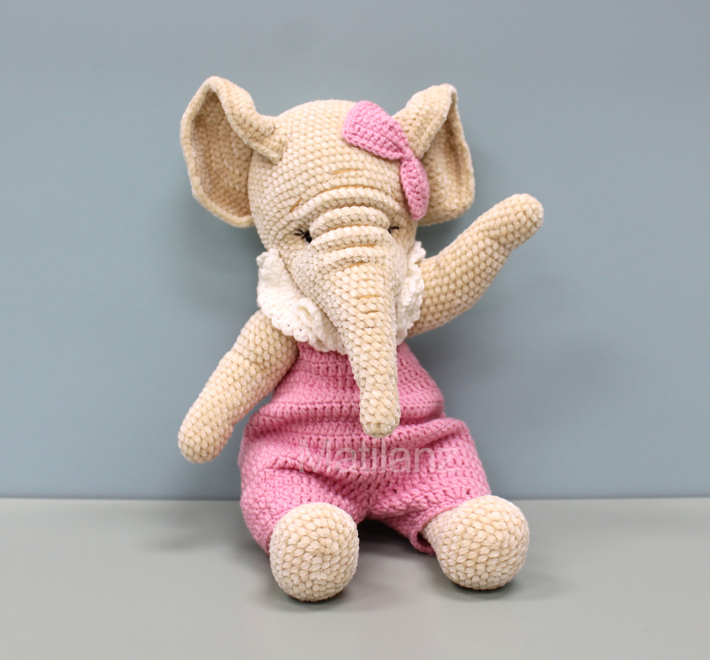 Crochet elephant in pink overalls with a pink bow, 13 inches tall.