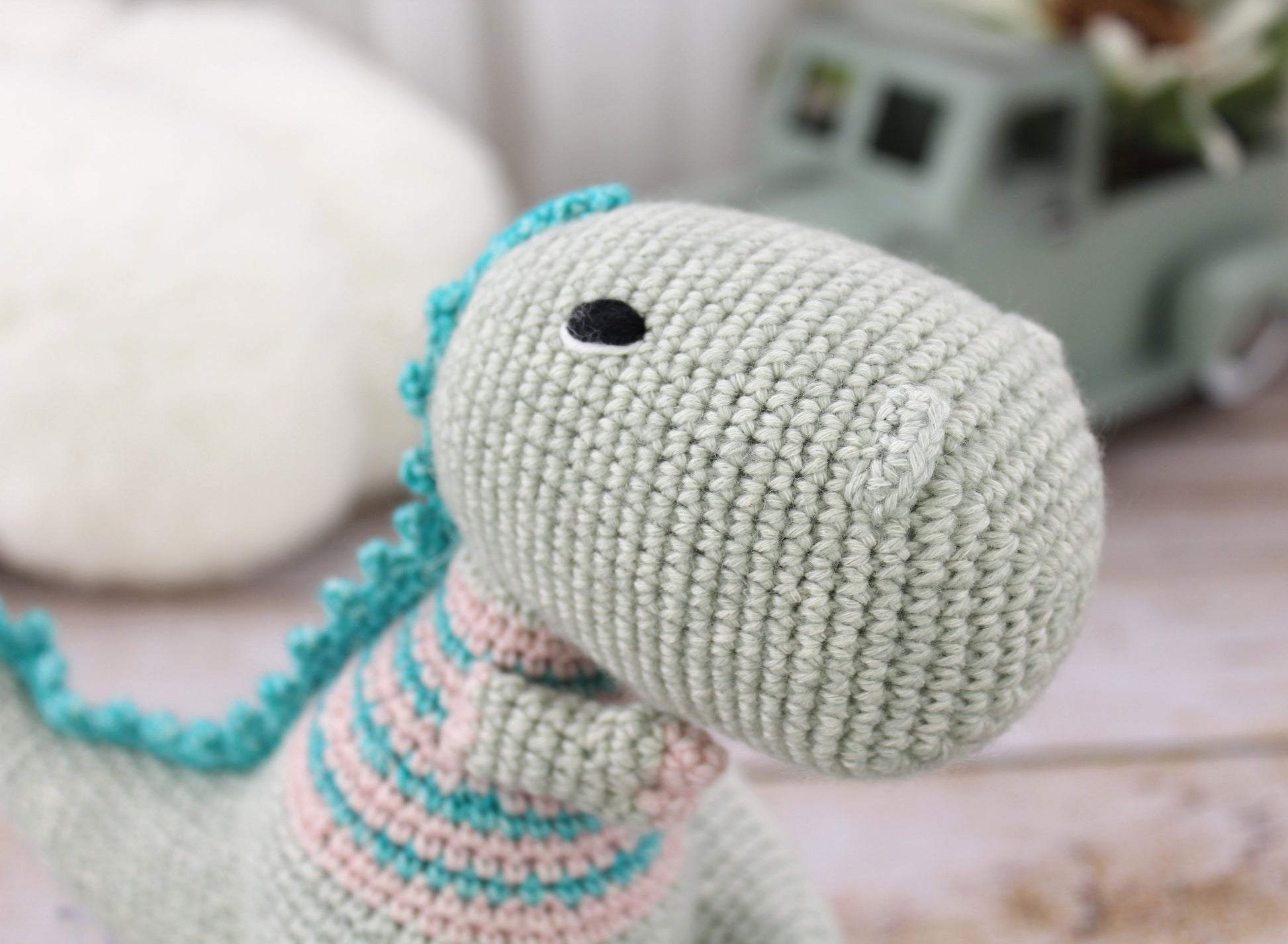 Handmade crochet T-rex plushie, light green with teal and pink accents, 8 inches tall.