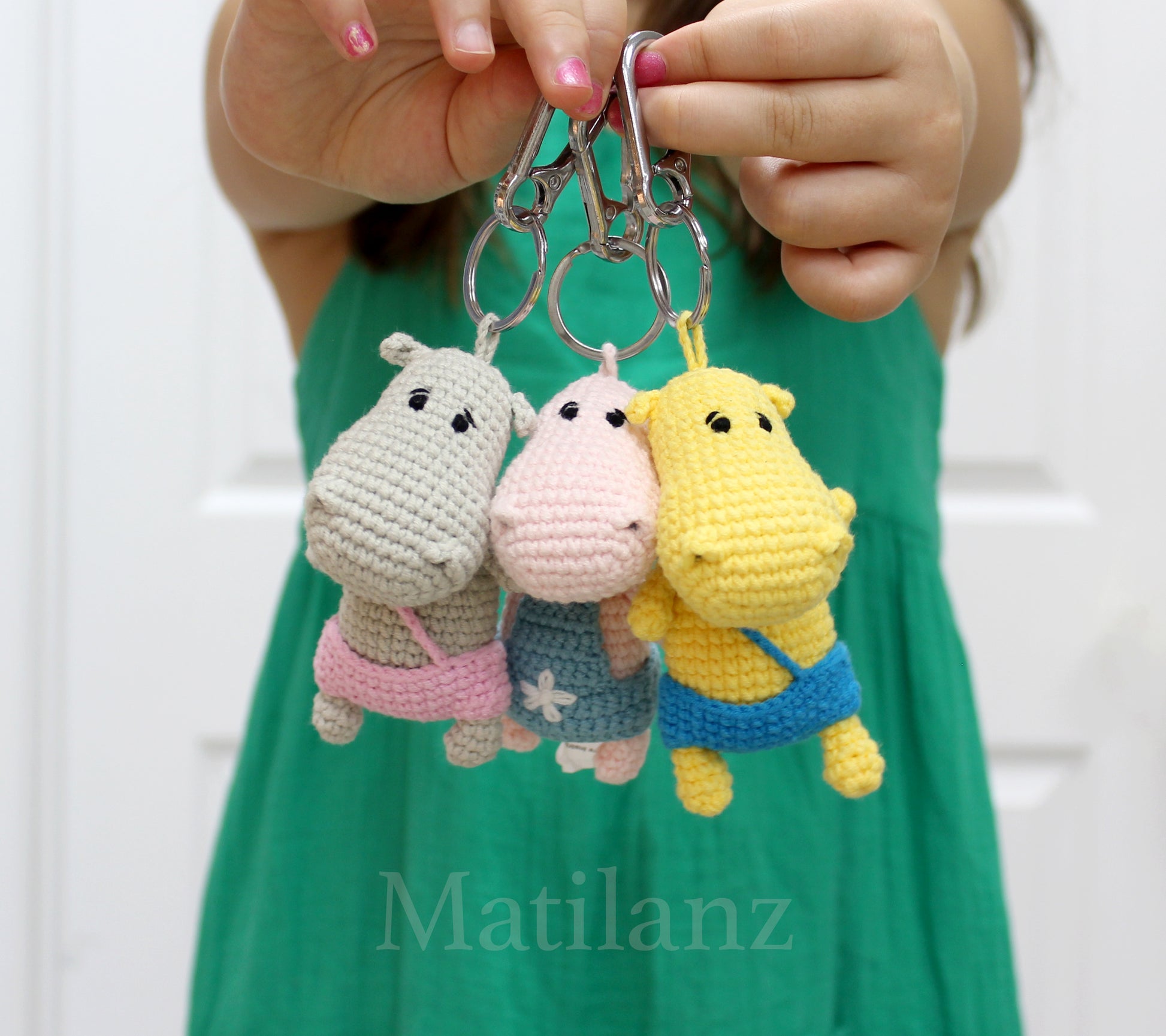Handmade crochet hippo keychains in gray, pink, and yellow, each with a colorful fabric band.