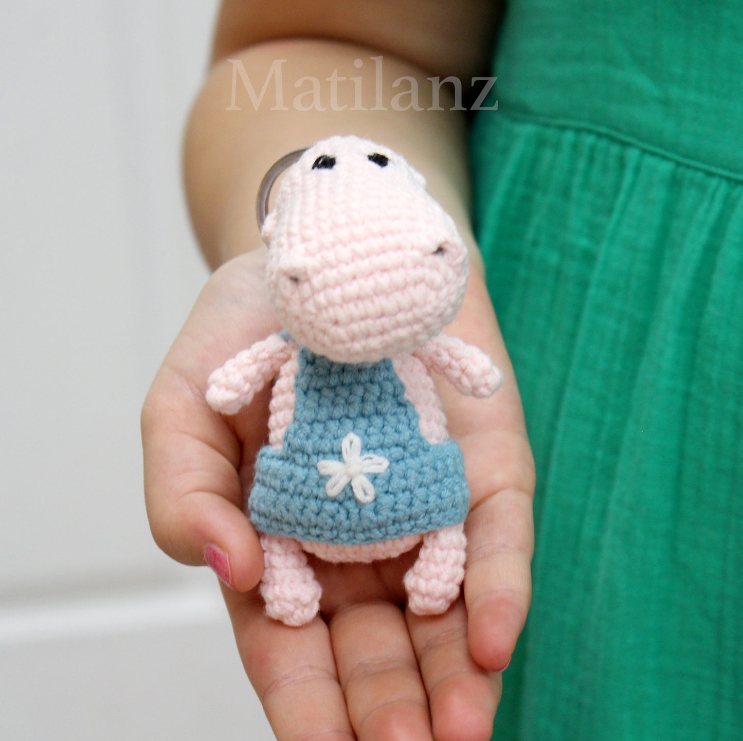 Handmade crochet hippo keychain in pink with a blue dress featuring a white flower.