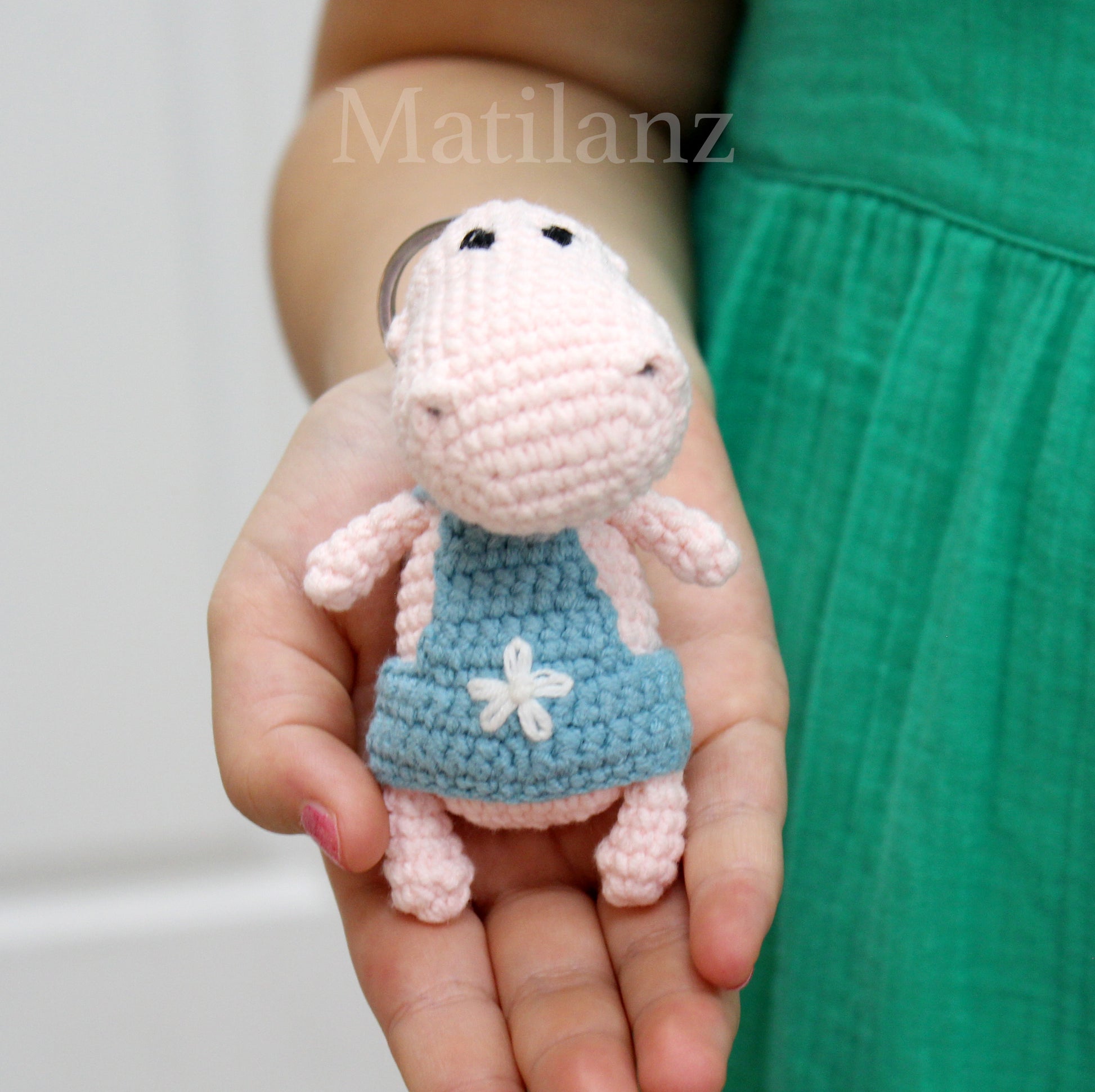 Handmade crochet hippo keychain in pink with a blue dress featuring a white flower.