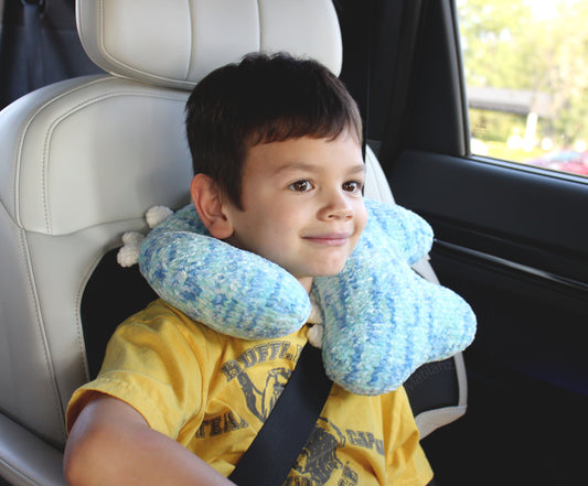 Handmade crochet dinosaur neck pillow in blue and white for children, providing comfort and support.