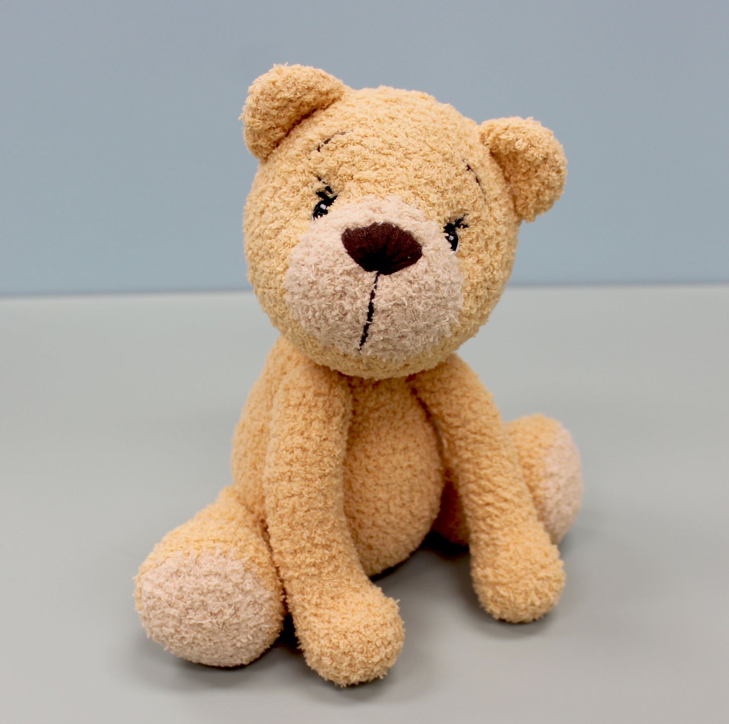 A beige crochet bear with a brown nose and embroidered eyes, sitting upright.
