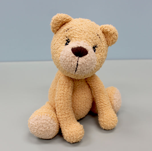 A beige crochet bear with a brown nose and embroidered eyes, sitting upright.