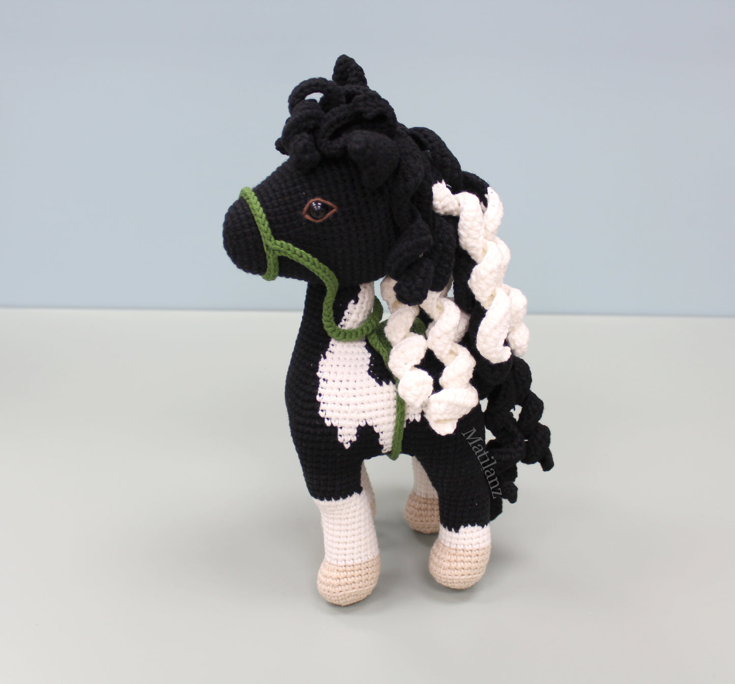 A handmade crochet paint horse plush toy with black and white patterns, green accents, and a flowing mane.