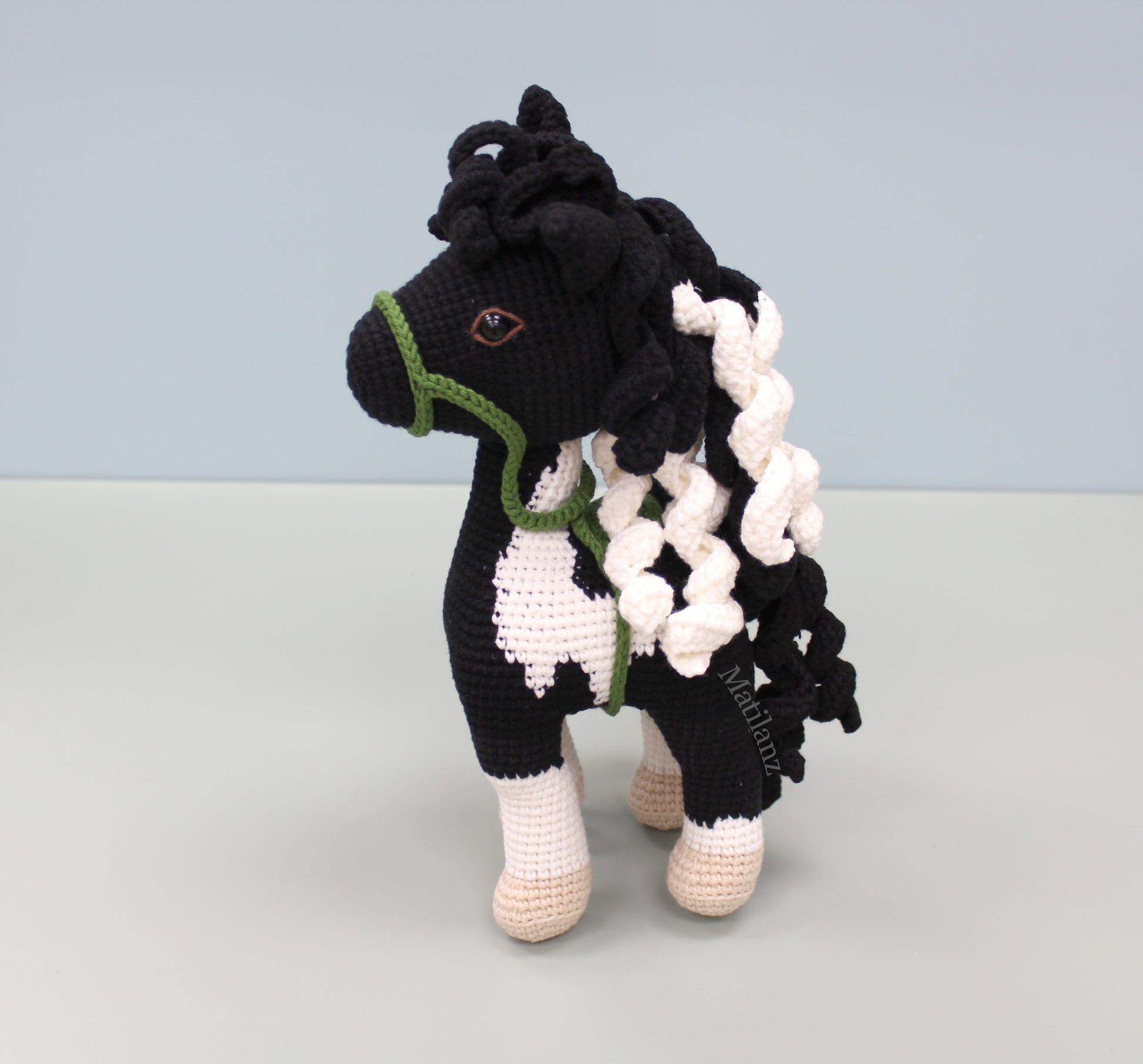 A handmade crochet paint horse plush toy with black and white patterns, green accents, and a flowing mane.