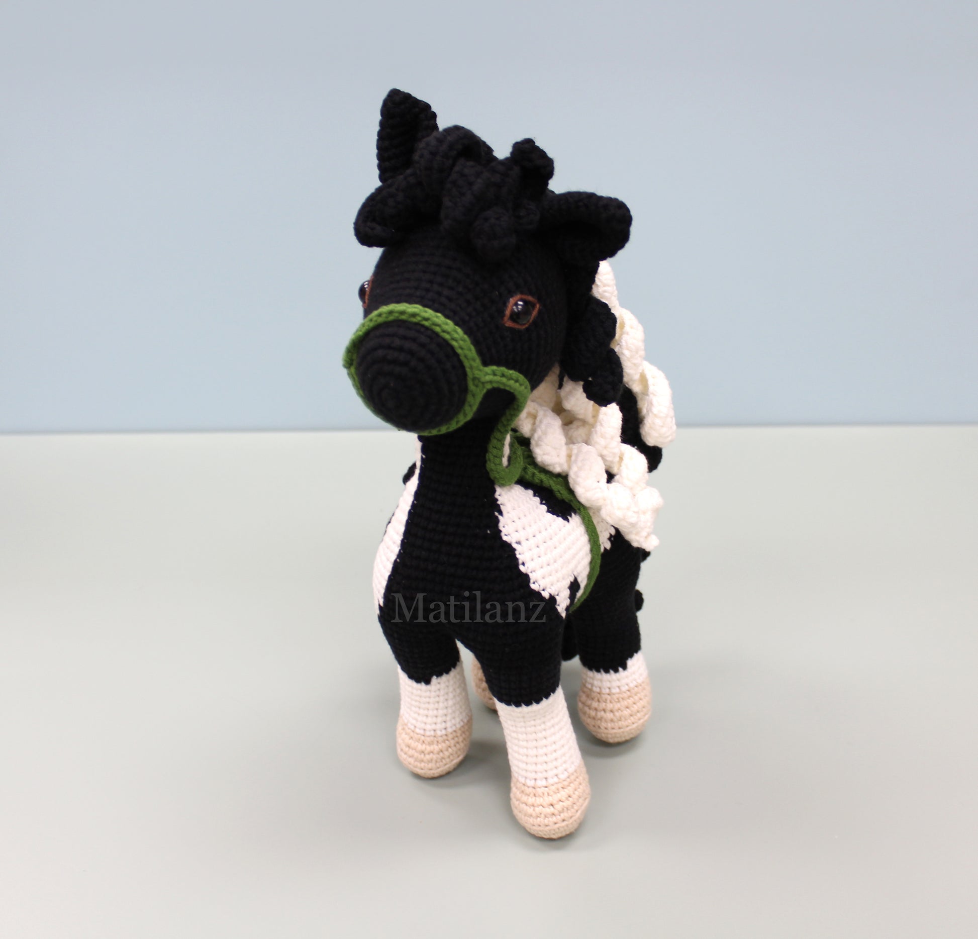 A handmade crochet paint horse plush toy with black and white stripes, green accents, and a small brown button.