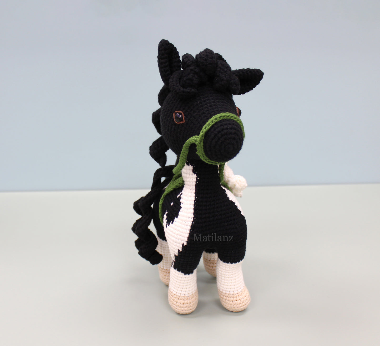 A handmade crochet paint horse plush toy with black and white stripes, green accents, and a braided mane.