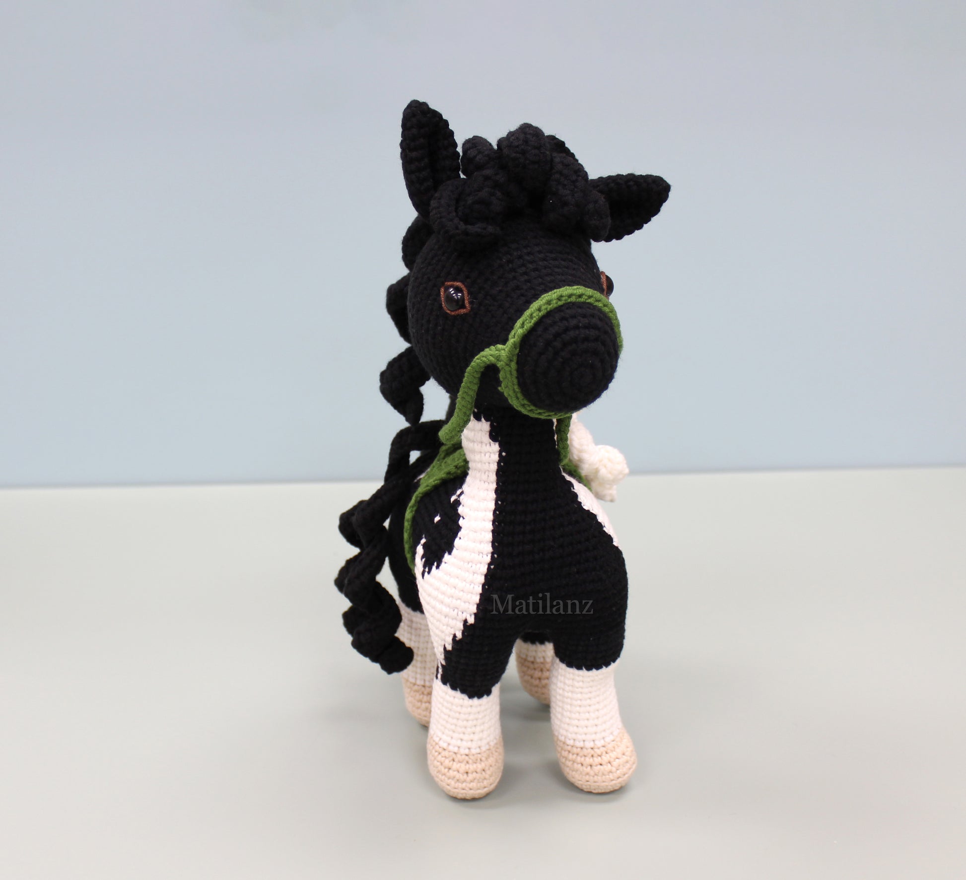 A handmade crochet paint horse plush toy with black and white stripes, green accents, and a braided mane.