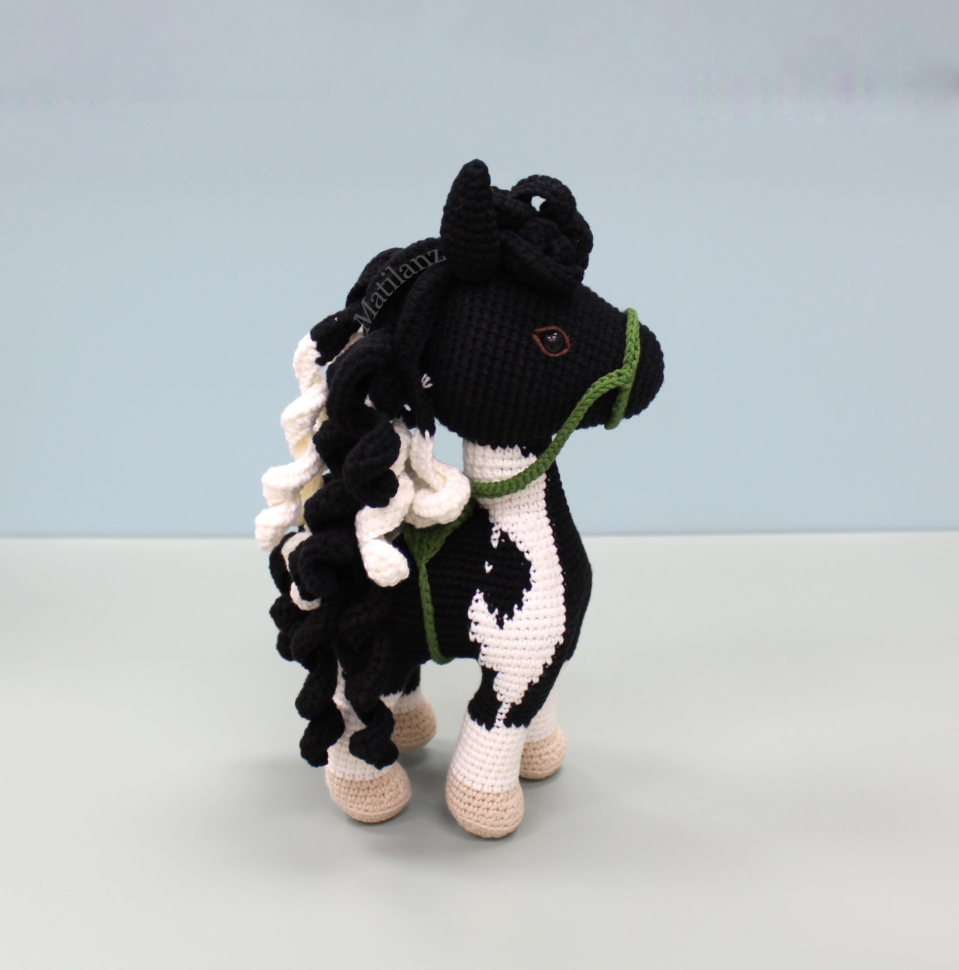 A handmade crochet paint horse plush toy with black and white patterns, green accents, and a flowing mane.