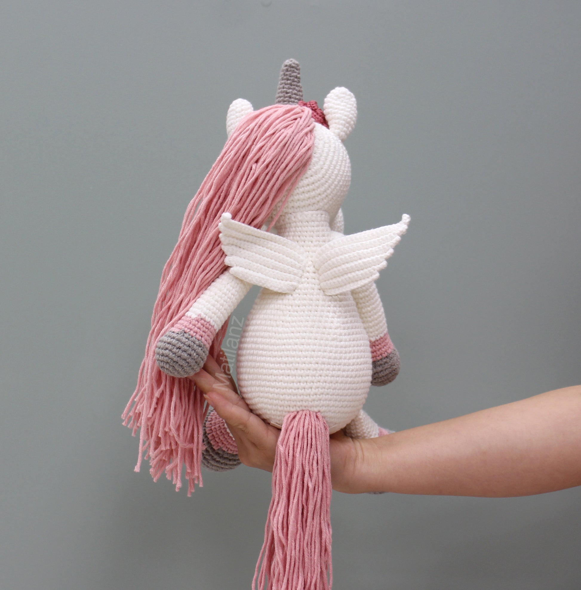 Handmade crochet unicorn horse with wings, white body, pink mane and tail, and gray hooves.