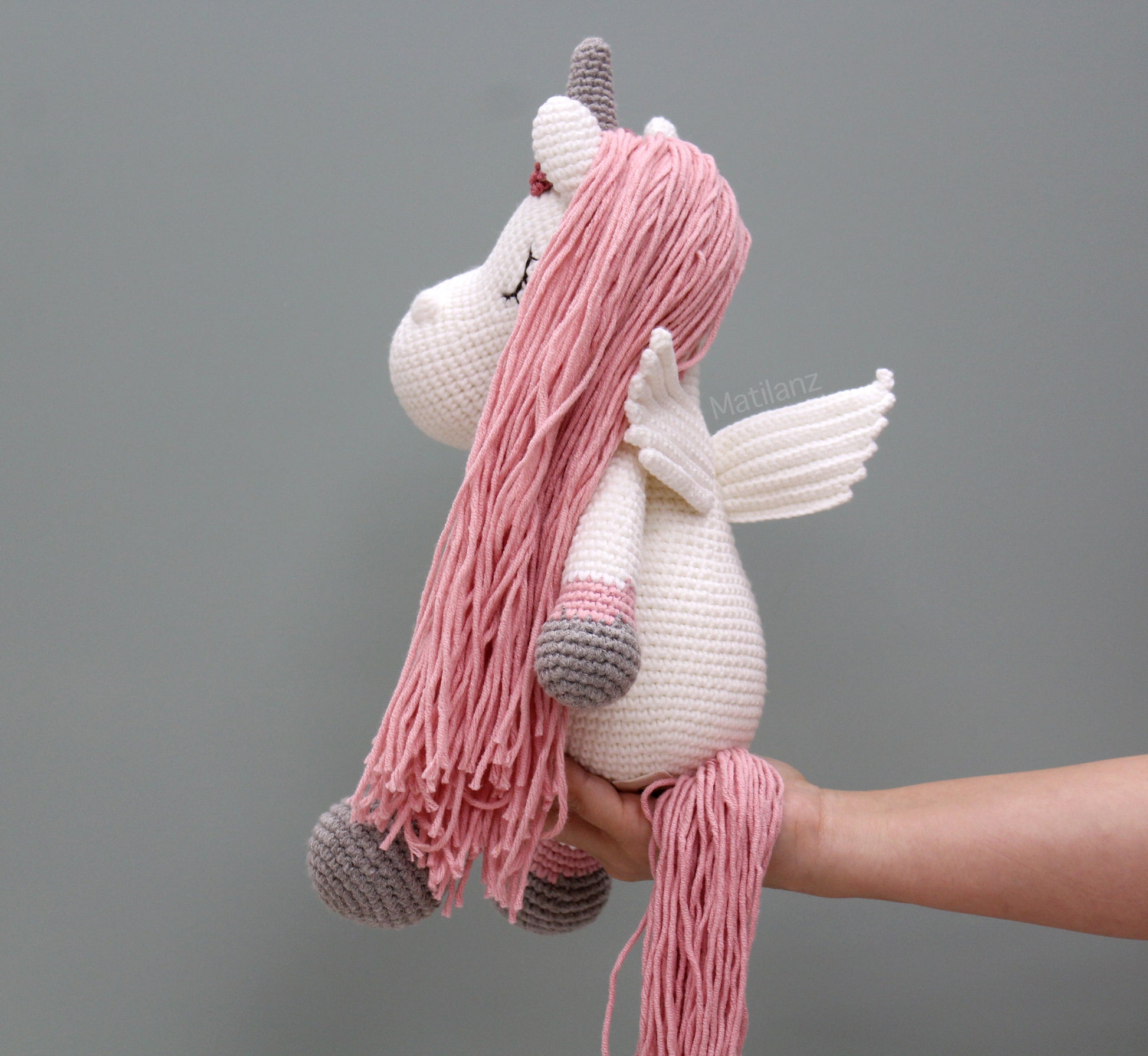 A handmade crocheted unicorn with pink mane, wings, and gray hooves, 14" tall.