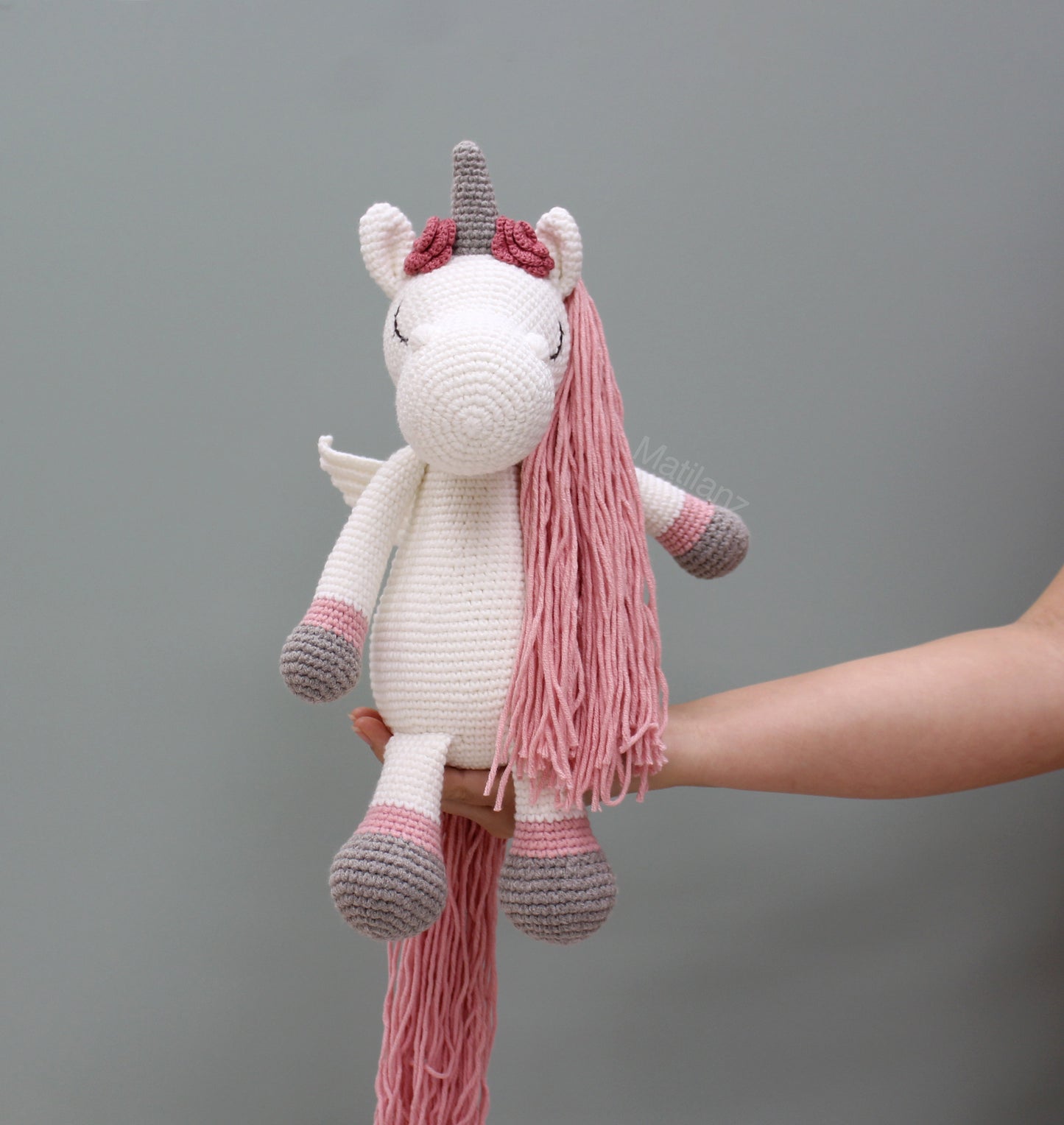 A handmade crochet unicorn with wings, pink mane, and gray horn, 14" tall.